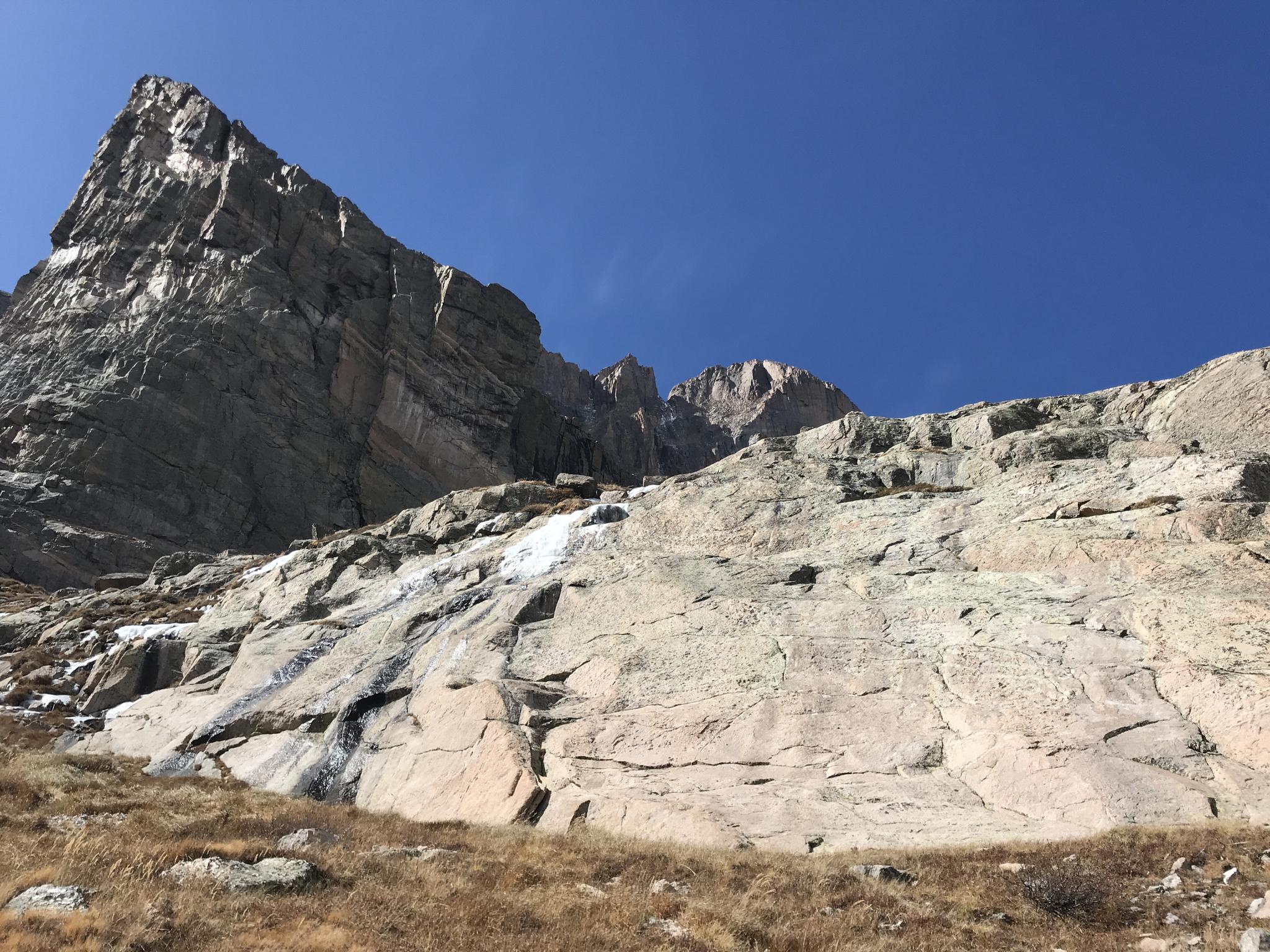 Towering rock face with patches of snow under a clear blue sky.