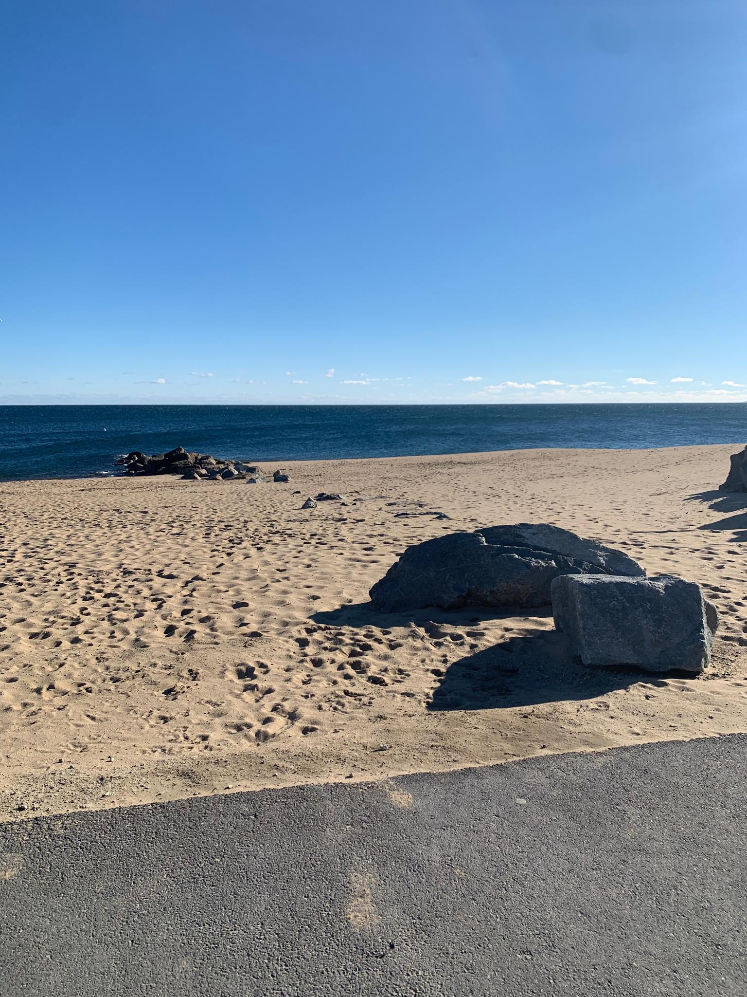 Sunny beach with large rocks, blue ocean, and clear sky.