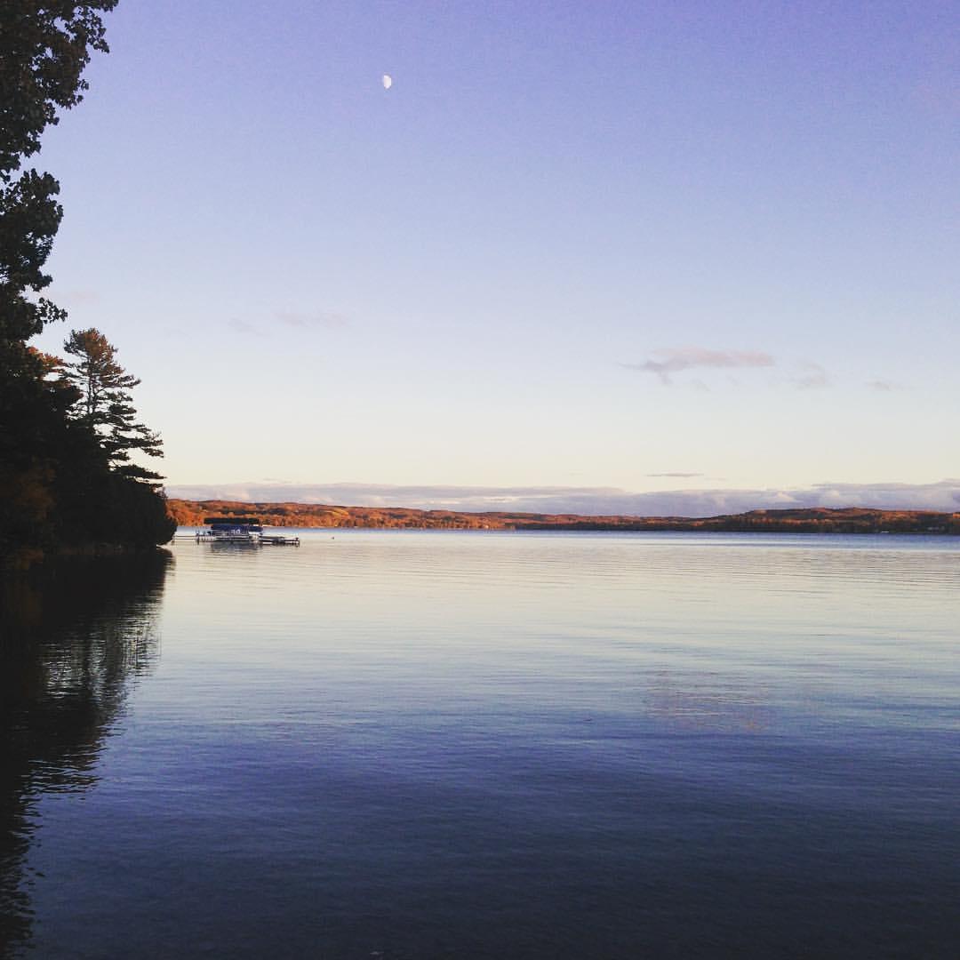 Calm lake water reflecting the sky, with a crescent moon visible.