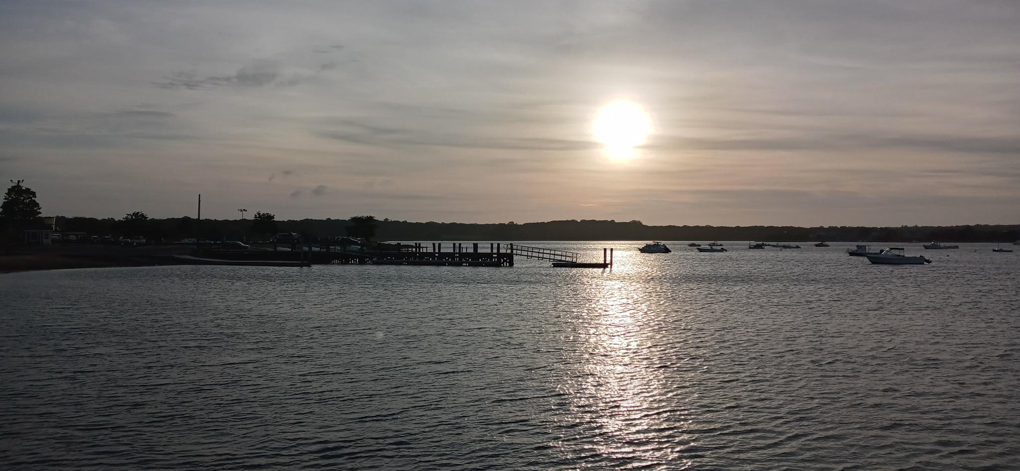 Sunset over a calm bay with a dock and several boats anchored.