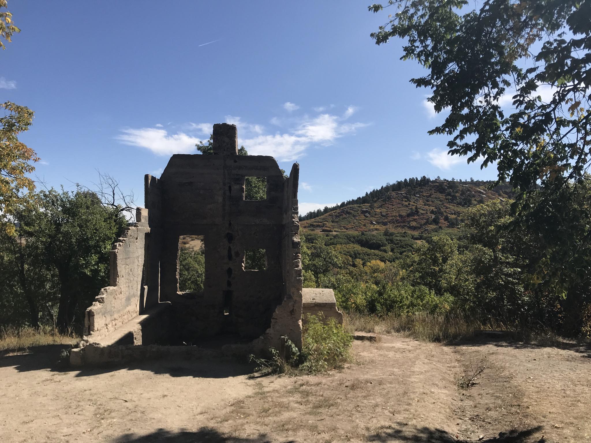 Stone ruins on a dirt path, surrounded by green trees under a blue sky.