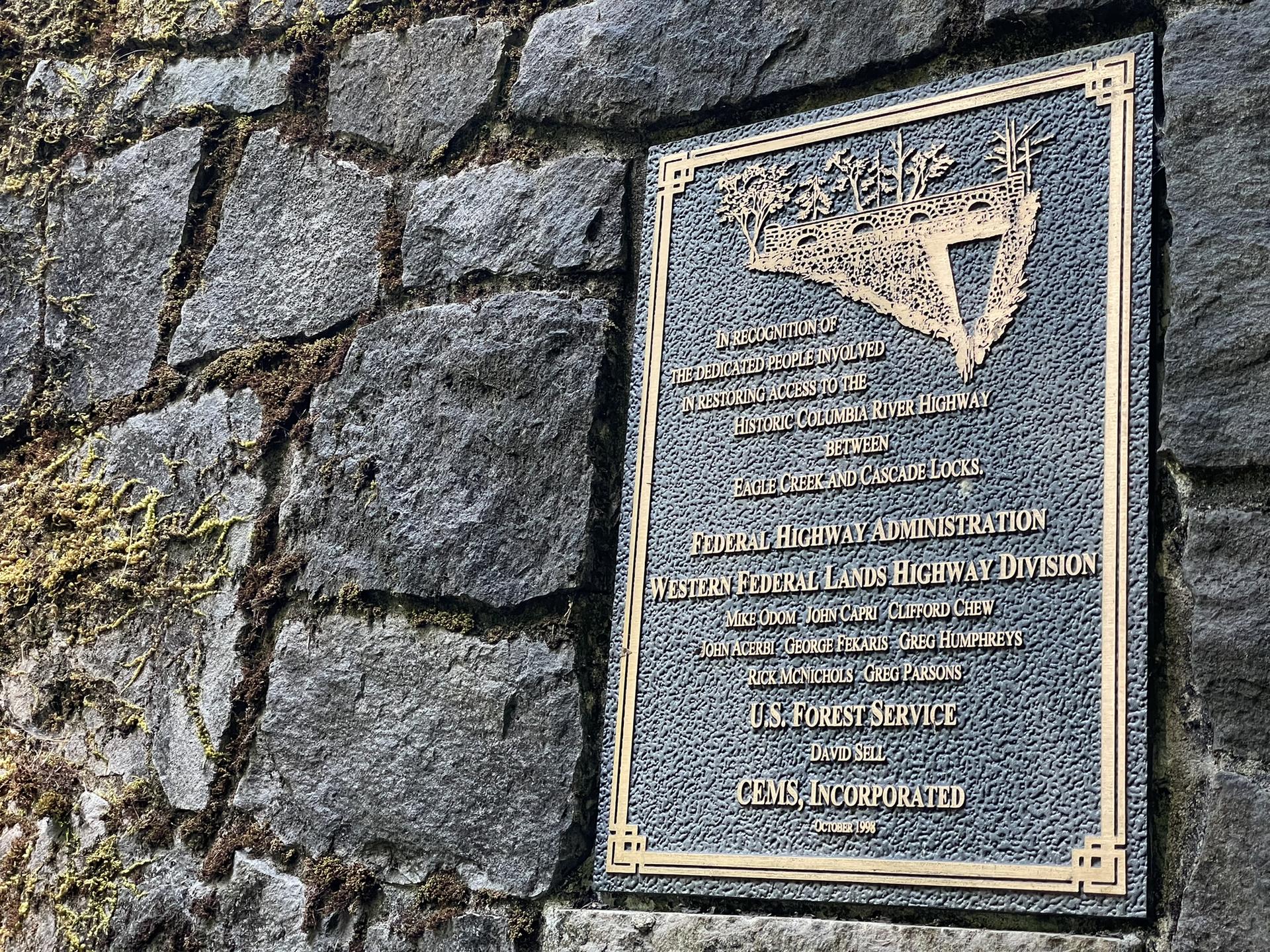 A bronze plaque with text mounted on a mossy stone wall.