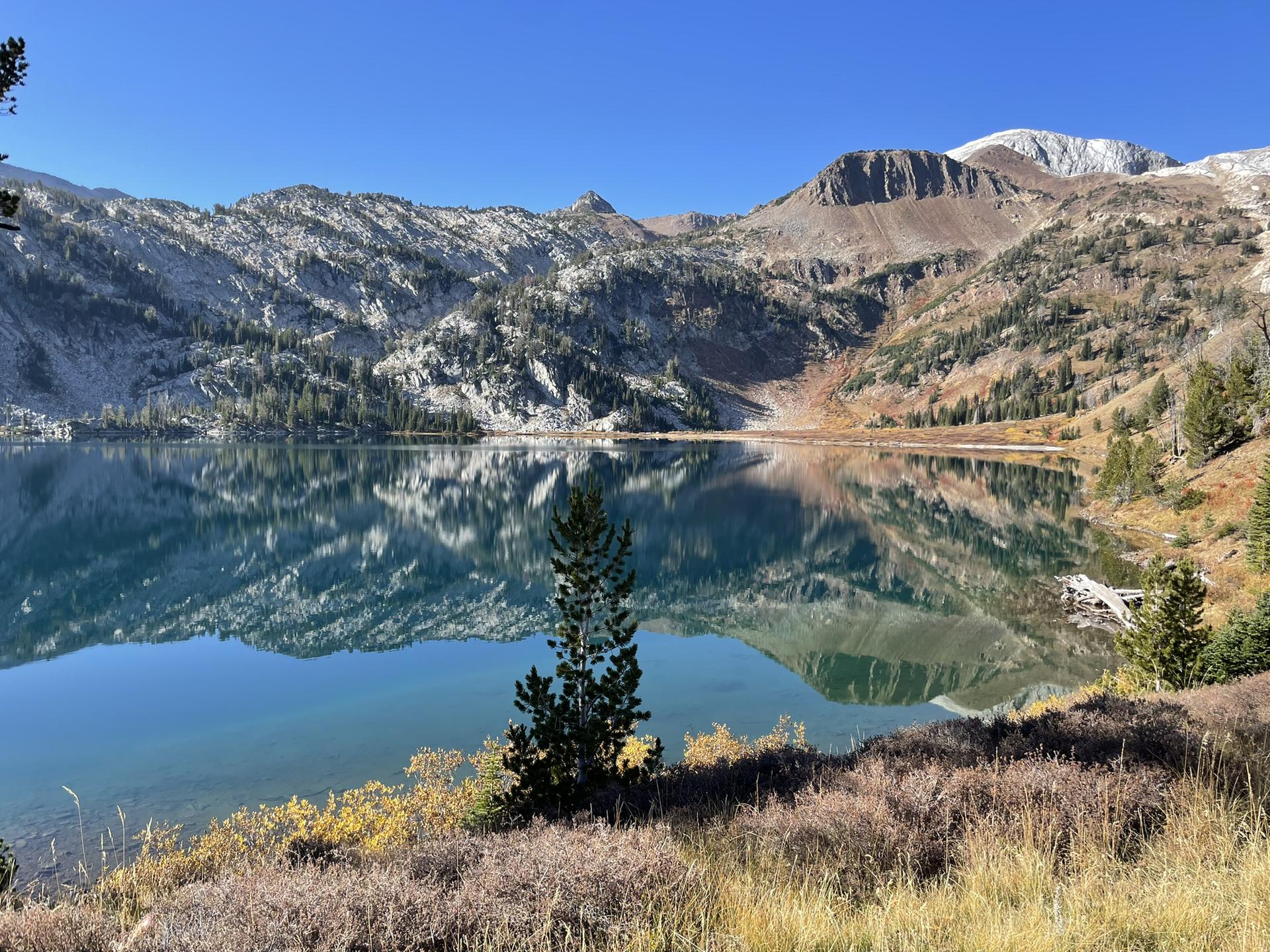 Clear mountain lake reflecting rugged peaks and blue sky on a sunny day.