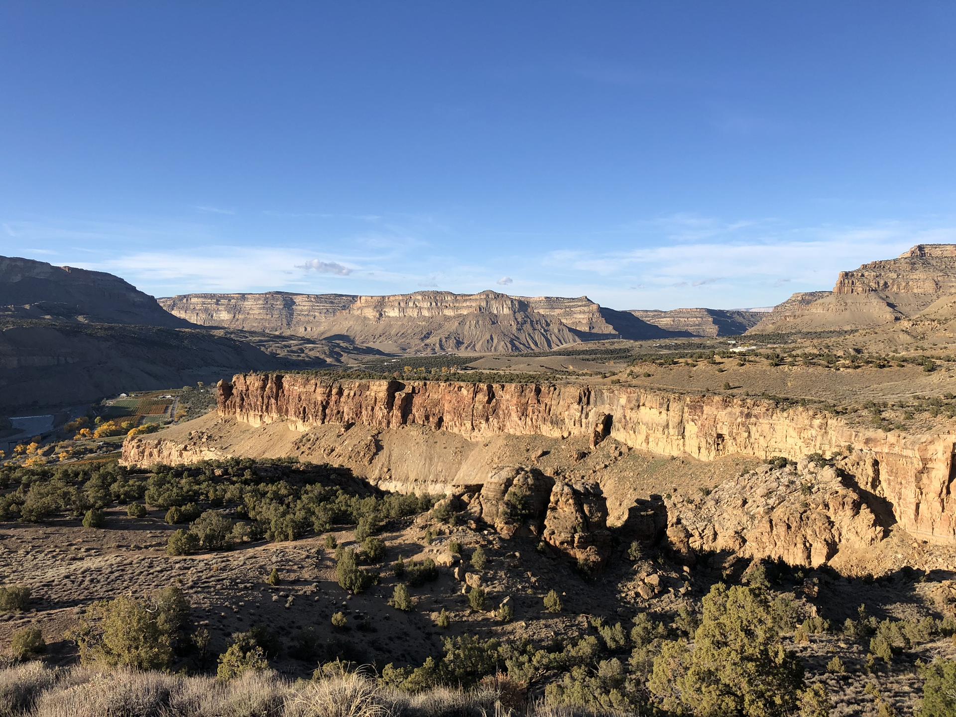 Sunny desert landscape with layered rock formations and distant mountains.