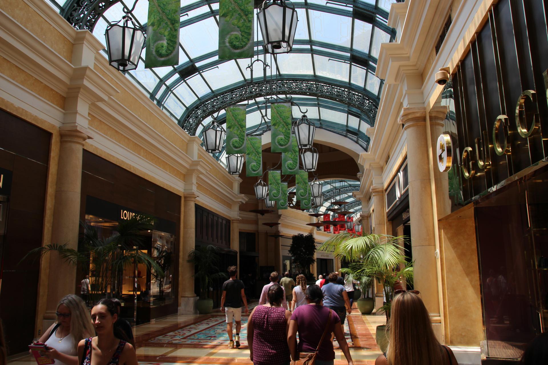 People stroll through an indoor shopping arcade with a glass ceiling and lanterns.