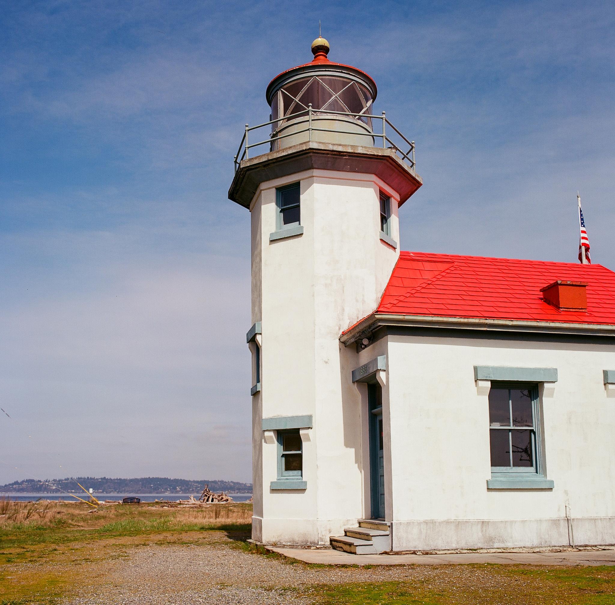 White lighthouse with a red roof under a bright blue sky, near water.