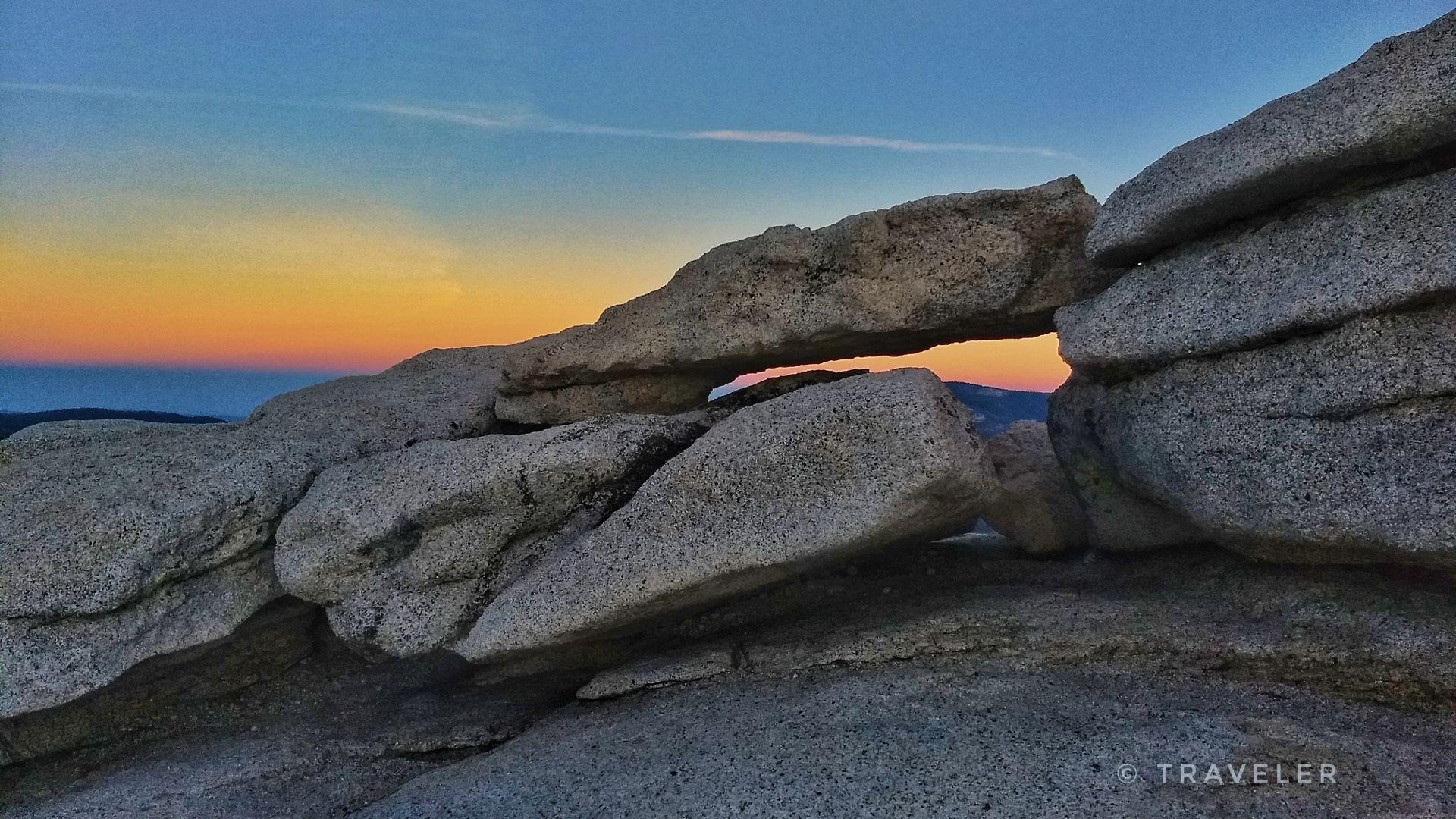 Natural rock arch silhouetted against a vibrant sunset sky.