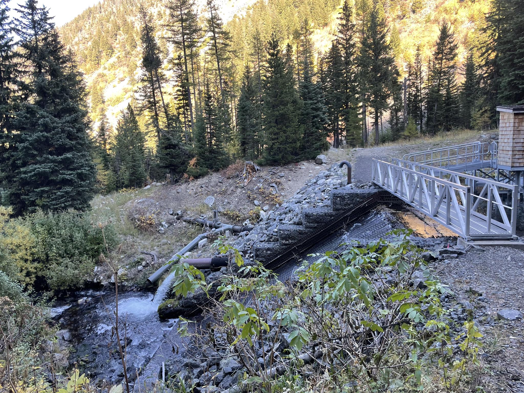 Industrial structure and bridge over a rocky stream in a forested valley.