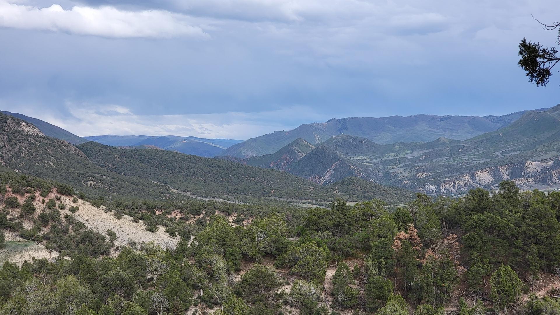 Expansive view of forested mountains and valleys under a dramatic cloudy sky.