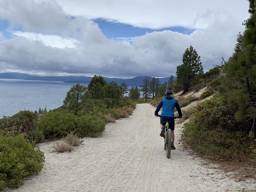 Person on a mountain bike rides a dirt path overlooking a large lake.