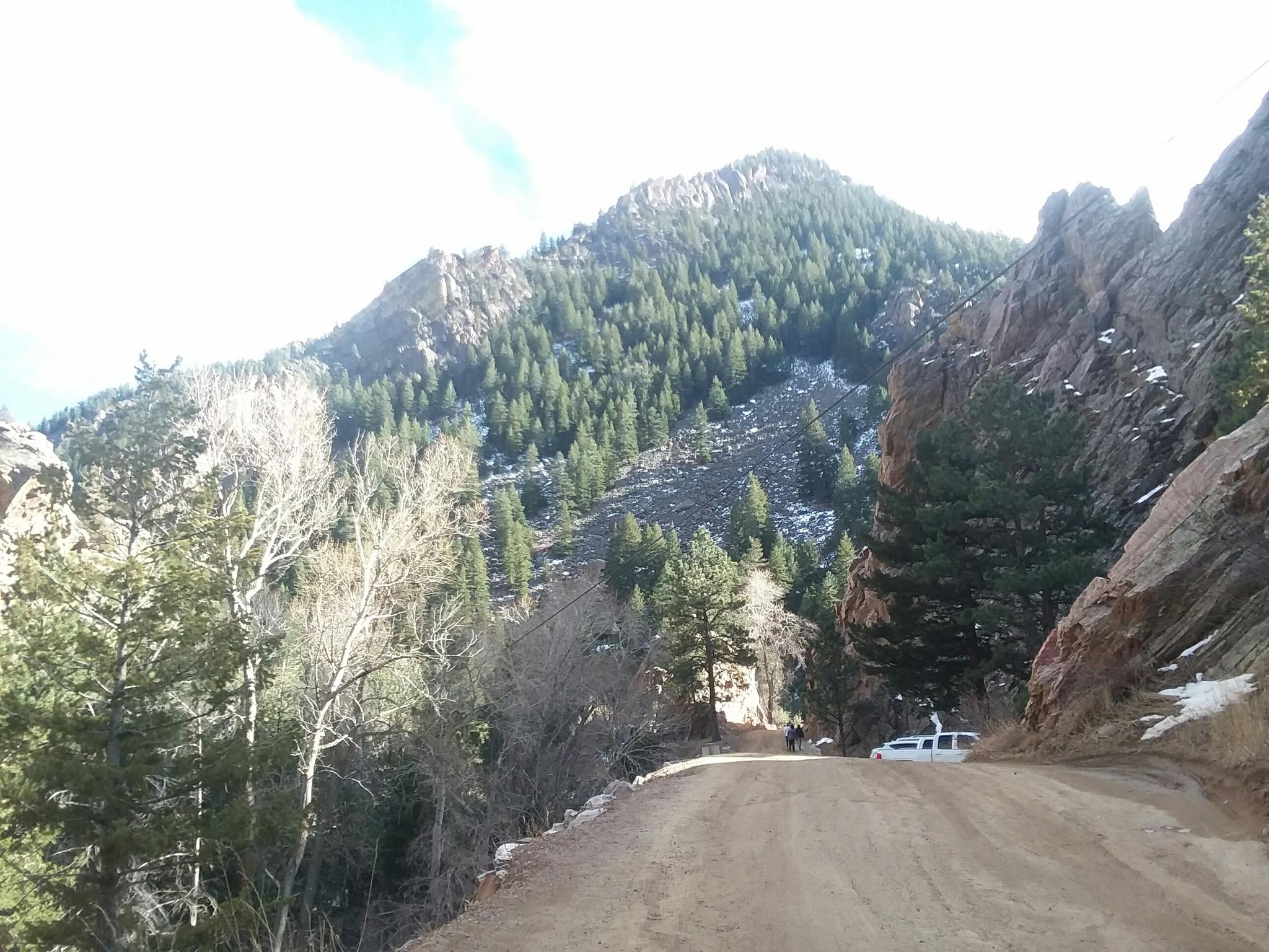 Dirt road winding through a valley with forested mountains and bright sky.