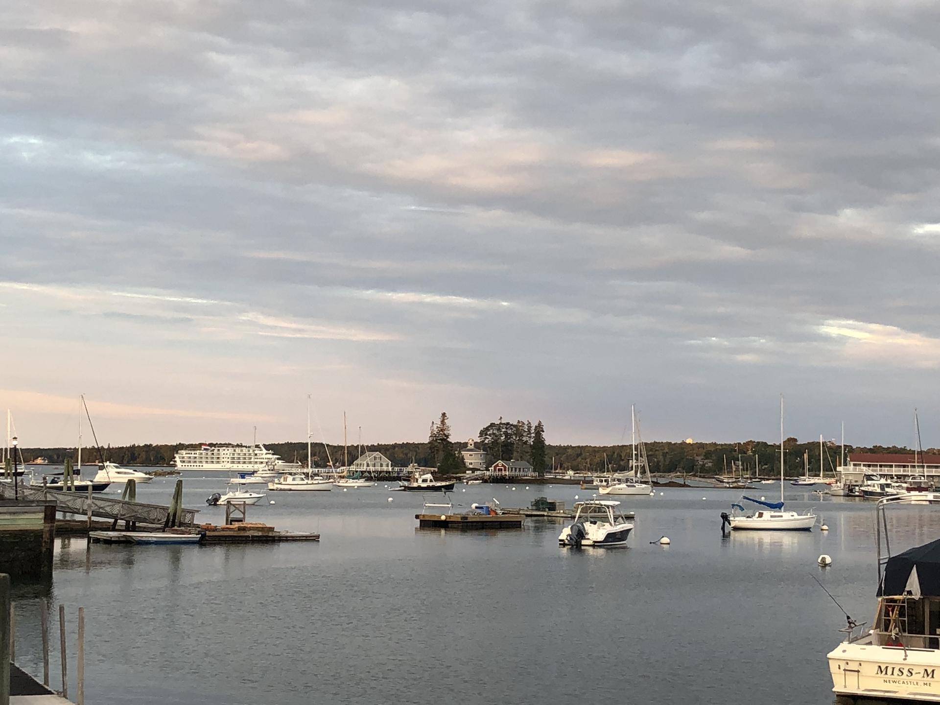 Numerous boats anchored in a wide harbor at dusk under cloudy skies.
