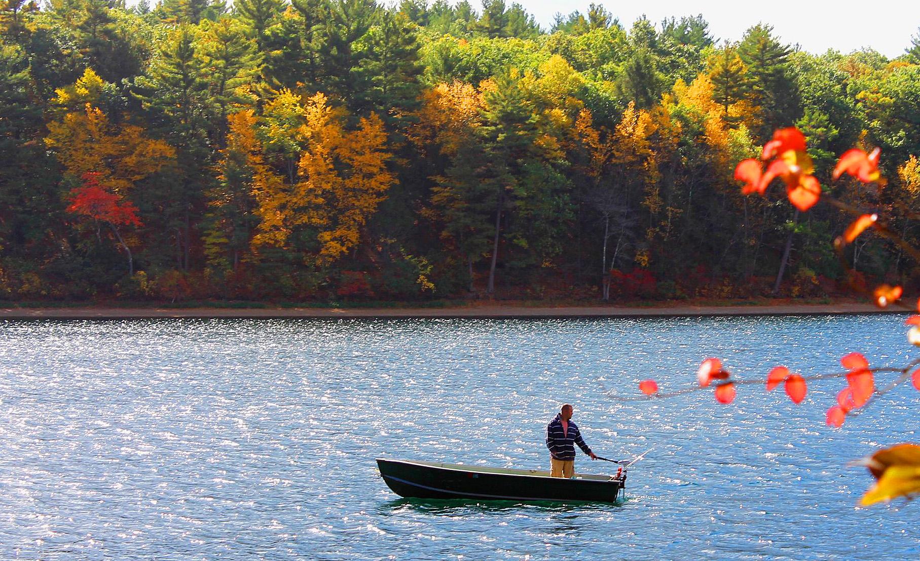 Person in a small boat on a lake with vibrant autumn trees.