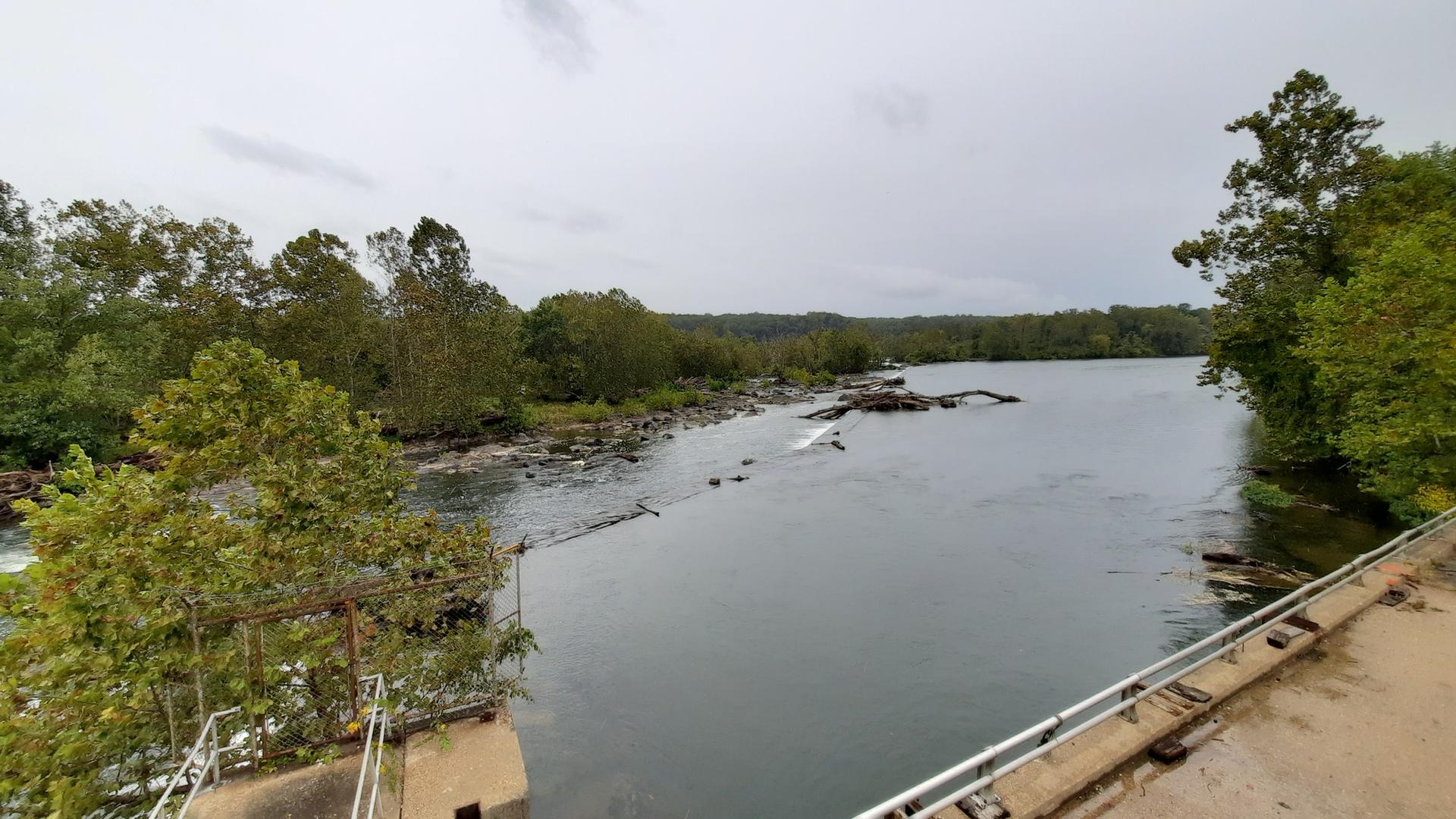 Wide river with rocky rapids, green trees, and a gray, overcast sky.