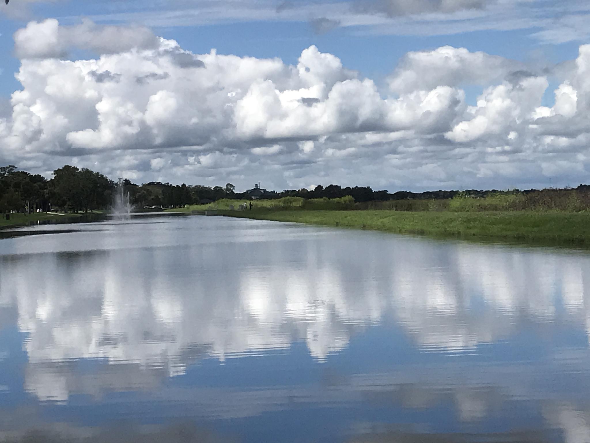 Wide canal reflecting a cloudy sky, flanked by green banks.