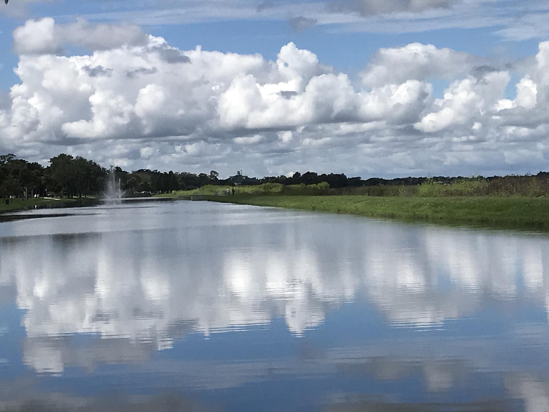 Wide canal reflecting a cloudy sky, flanked by green banks.