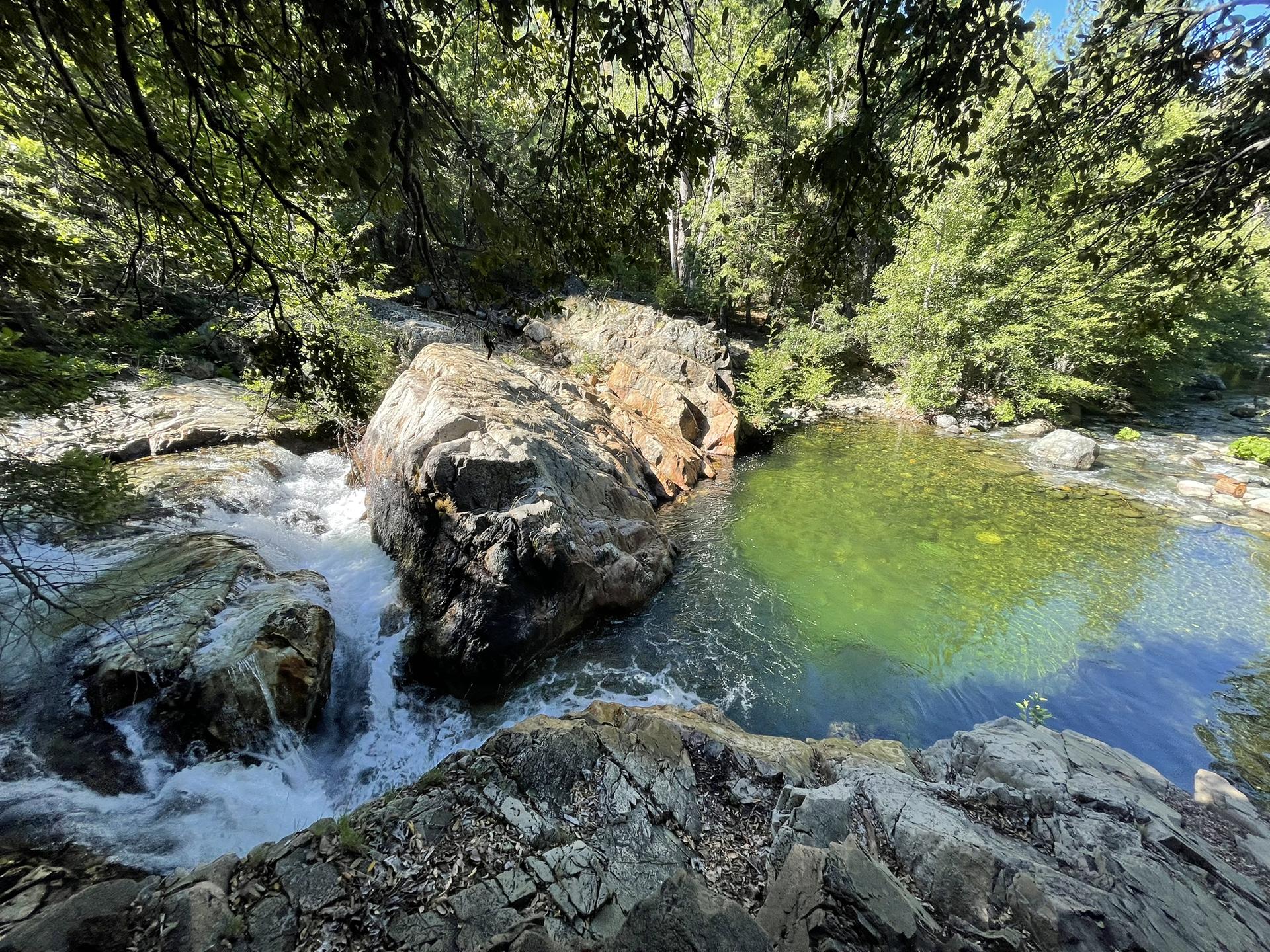 River cascades over rocks into a clear green pool surrounded by forest.
