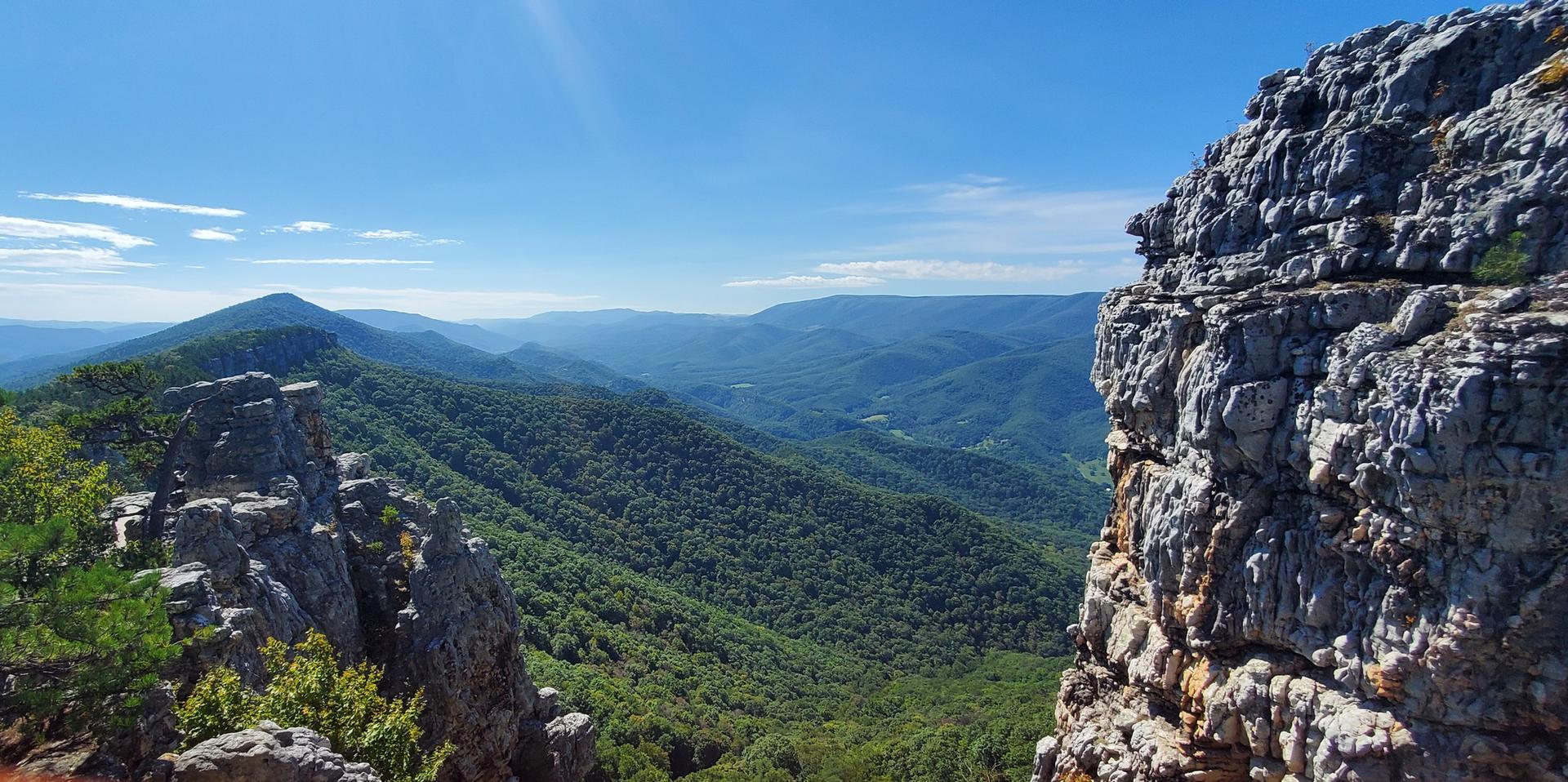 Expansive mountain vista with green valleys and rocky cliffs under a bright sky.