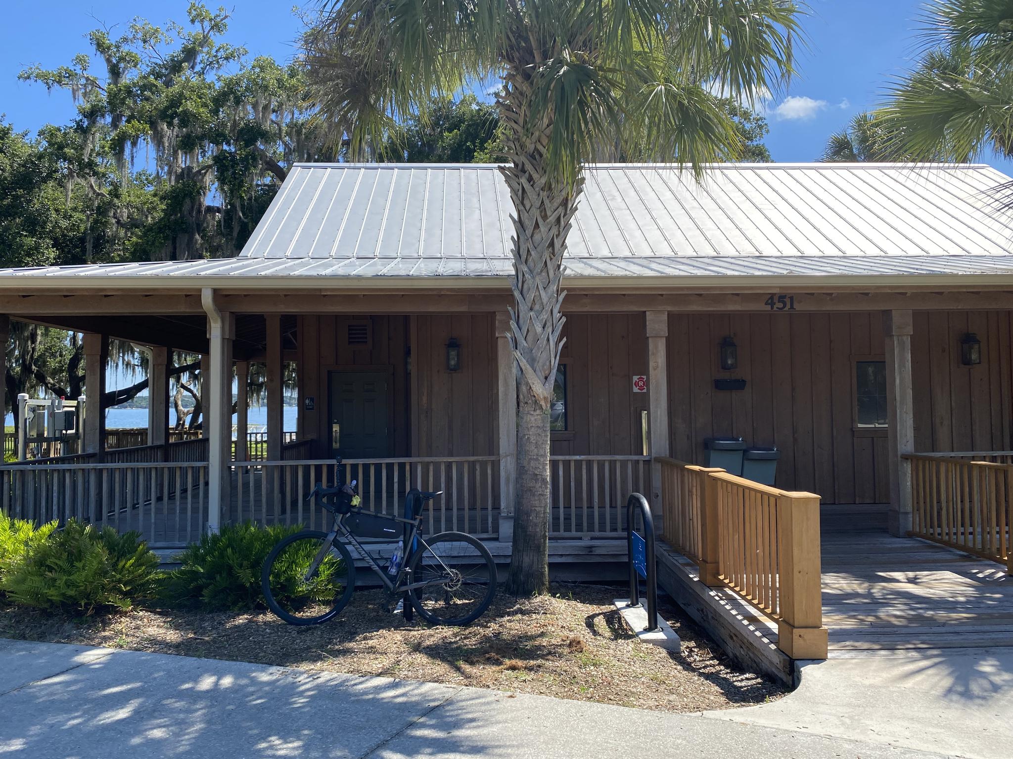 Sunny wooden building with a metal roof, a palm tree, and a parked bicycle.