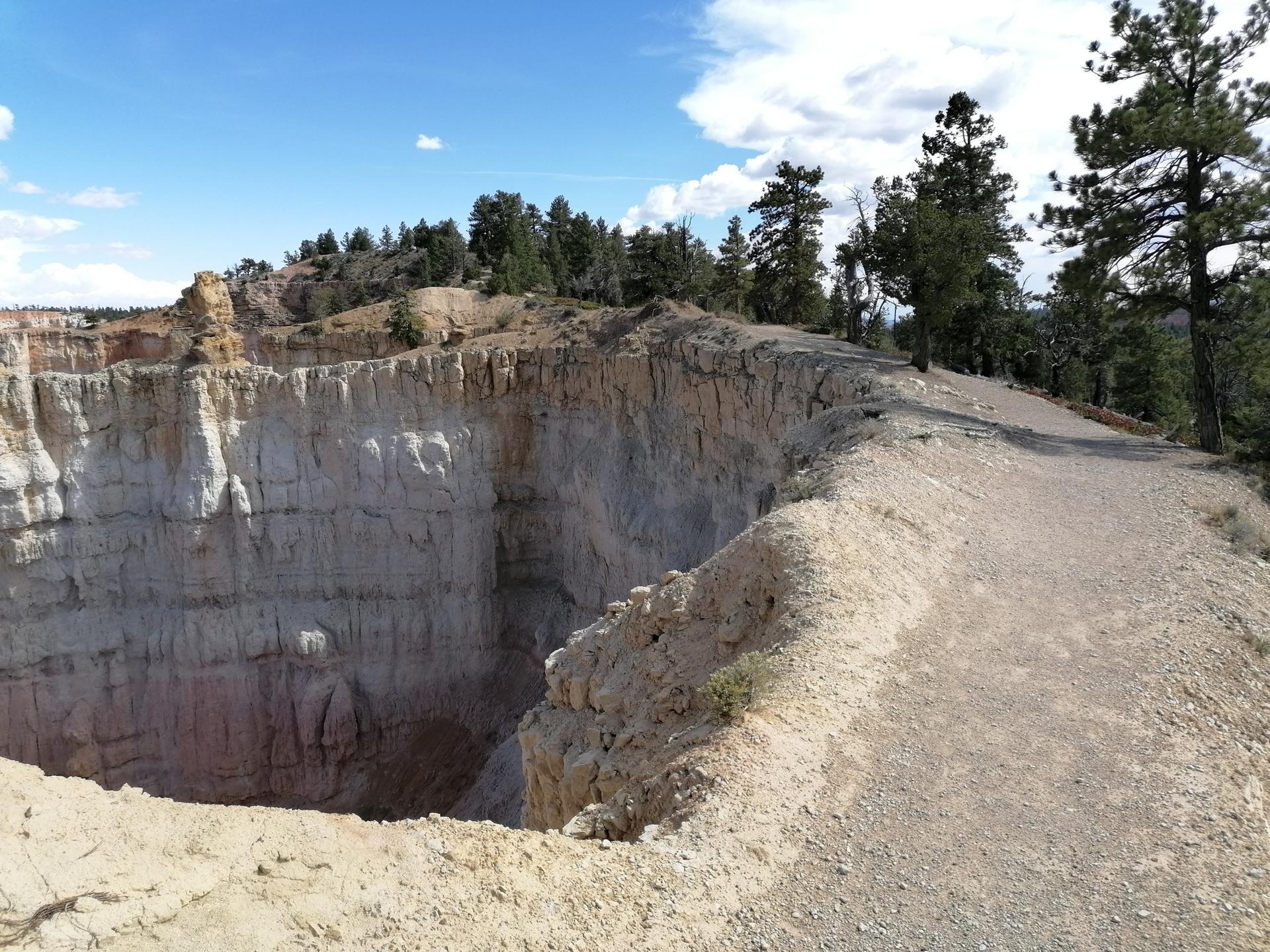 Dirt path winding along a steep canyon edge under a bright blue sky.
