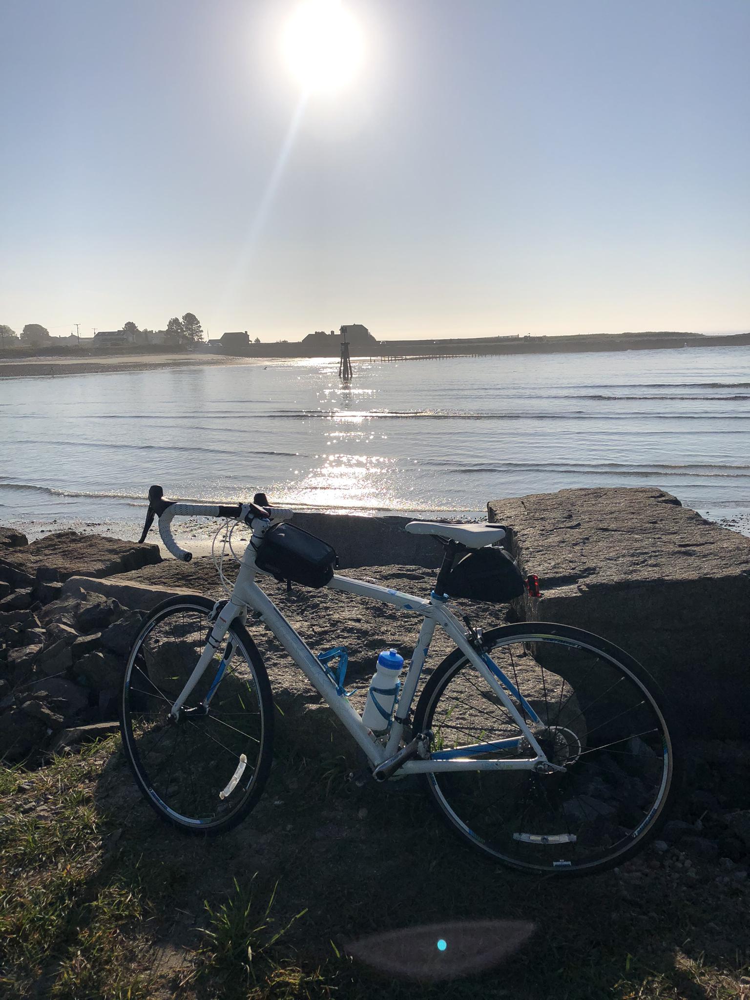 Bicycle parked on a rocky shore with bright sun reflecting on the ocean.