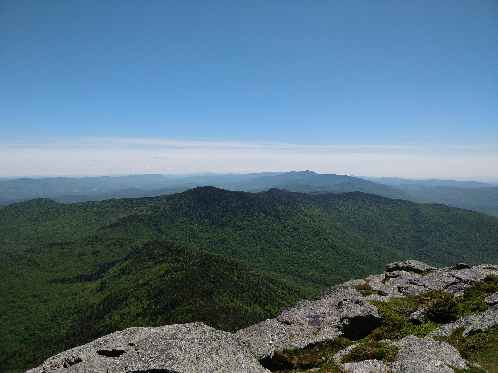 Expansive mountain range covered in green trees under a clear blue sky.