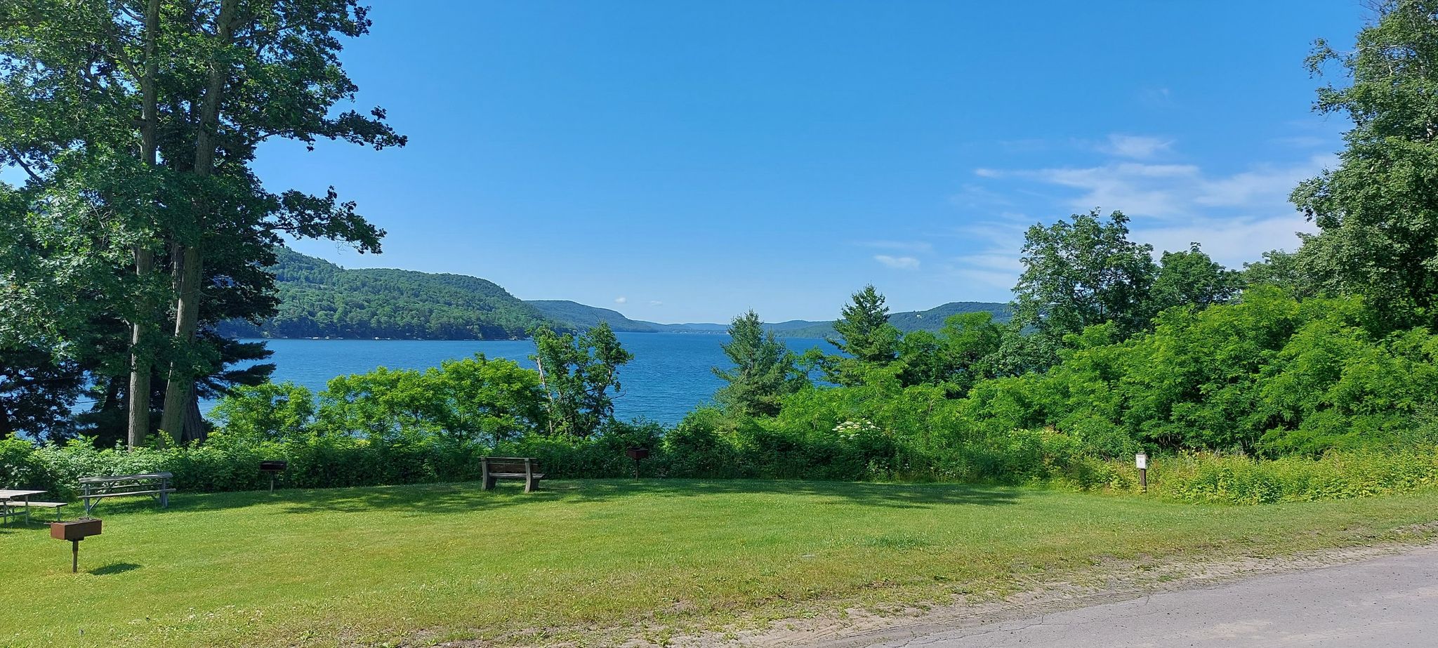 Sunny view of a large lake and forested mountains from a grassy recreational area. - Sleeping Lion Trail