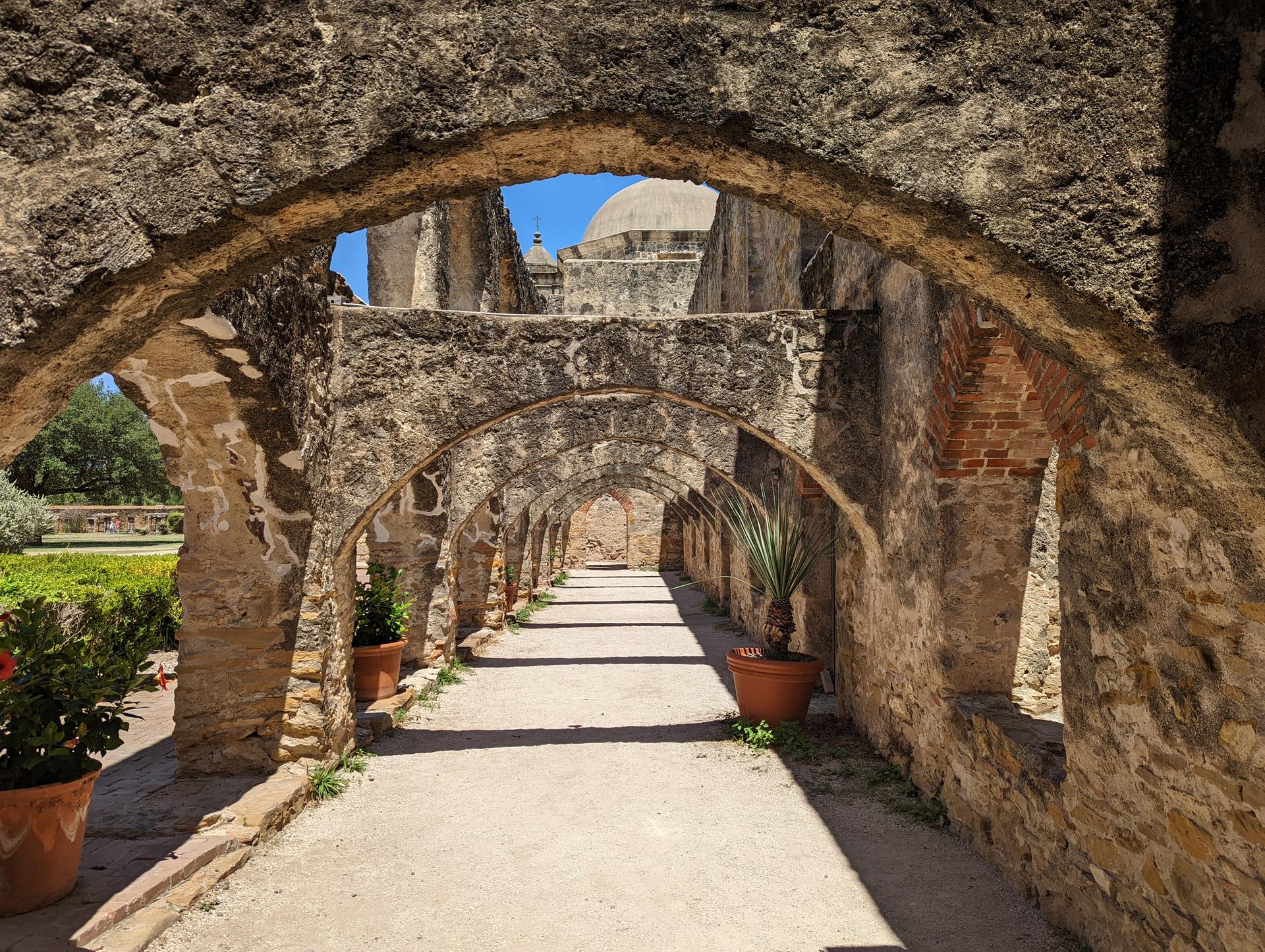 Long stone archway with potted plants, leading to a distant dome.