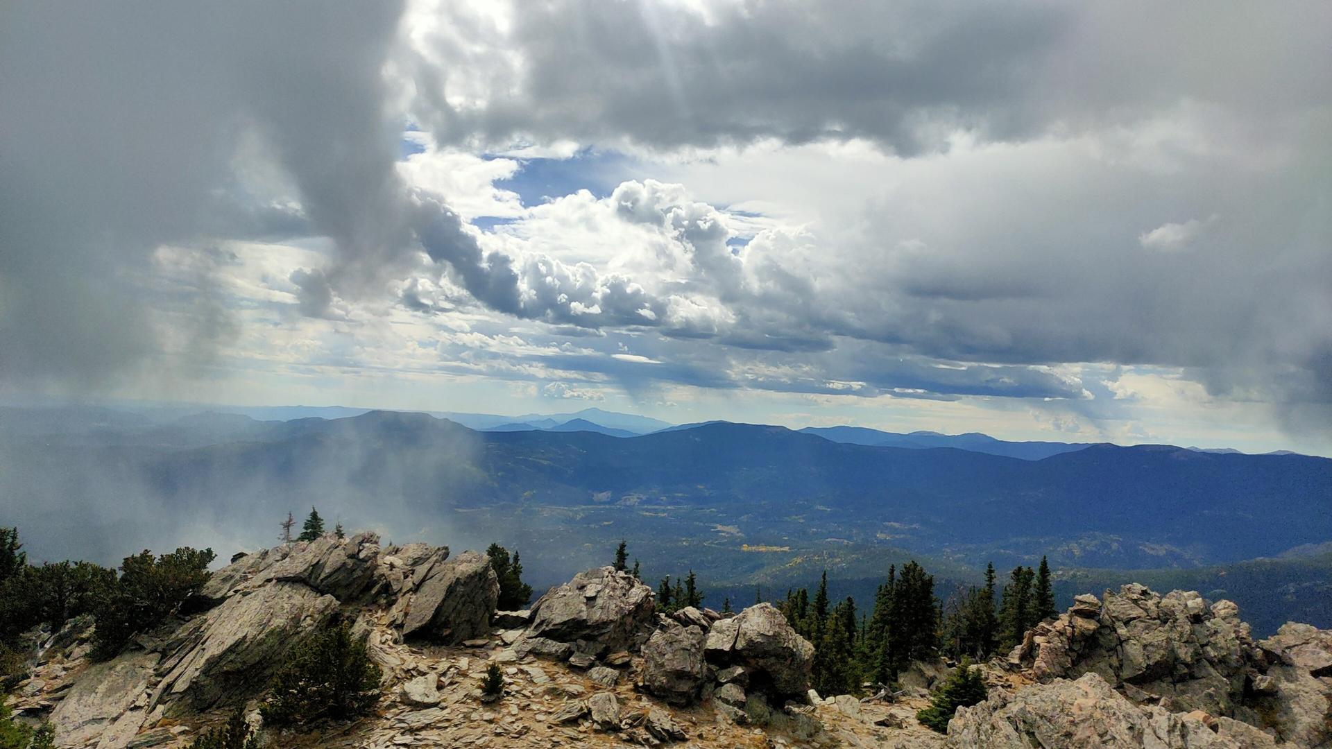 Dramatic cloudy sky over a rocky mountain peak and hazy distant landscape.