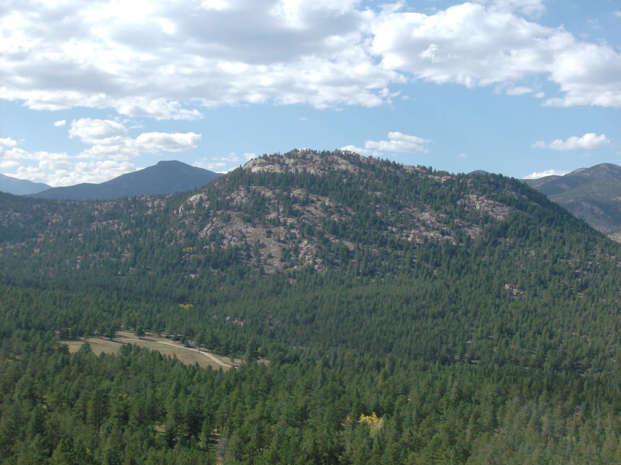 Expansive view of a forested mountain under a partly cloudy sky.