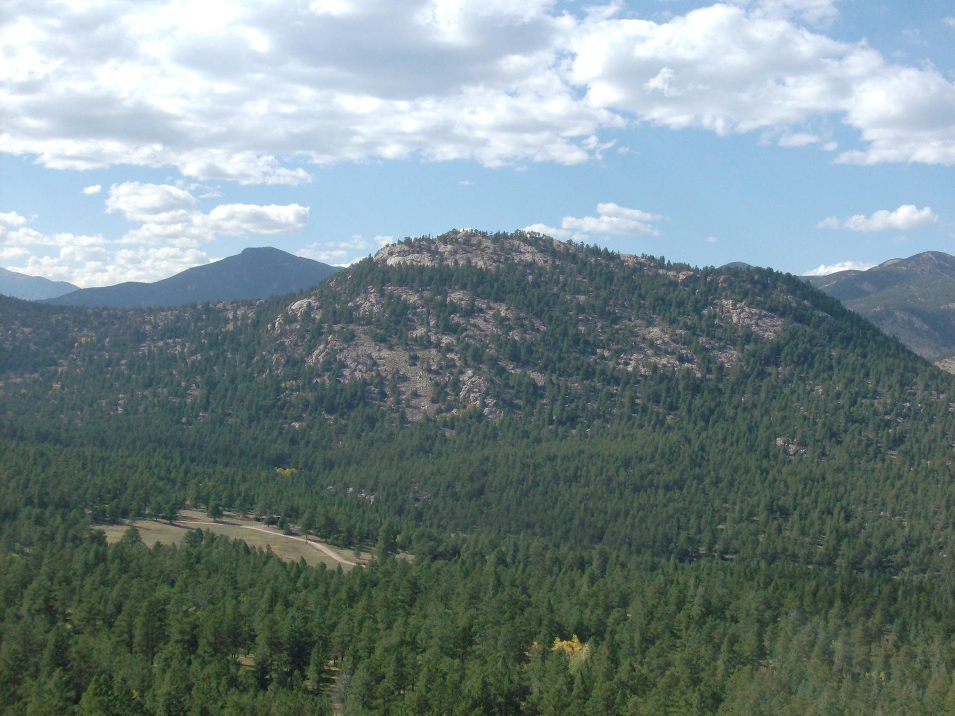 Expansive view of a forested mountain under a partly cloudy sky.