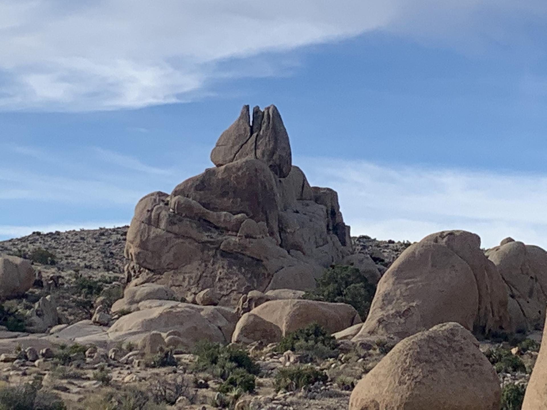 Tall, split rock formation rises from a rocky desert landscape under a blue sky.
