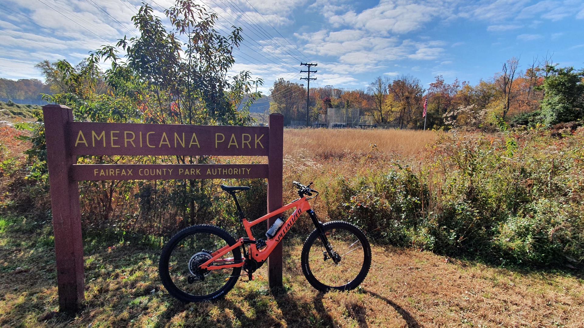 An orange mountain bike parked next to a wooden sign in a field.