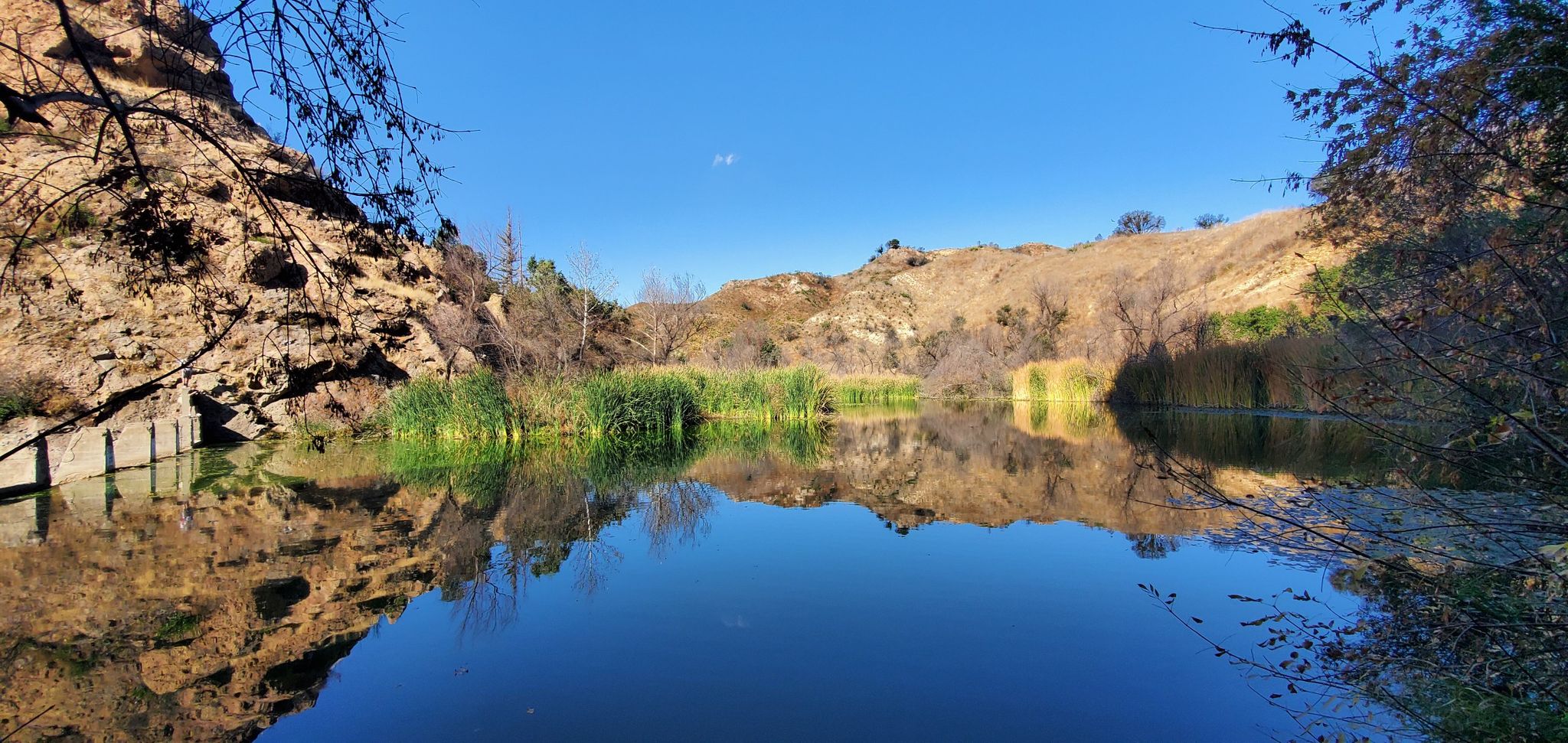Calm lake reflecting hills and reeds under a bright blue sky. - Crags Road and High Road Loop