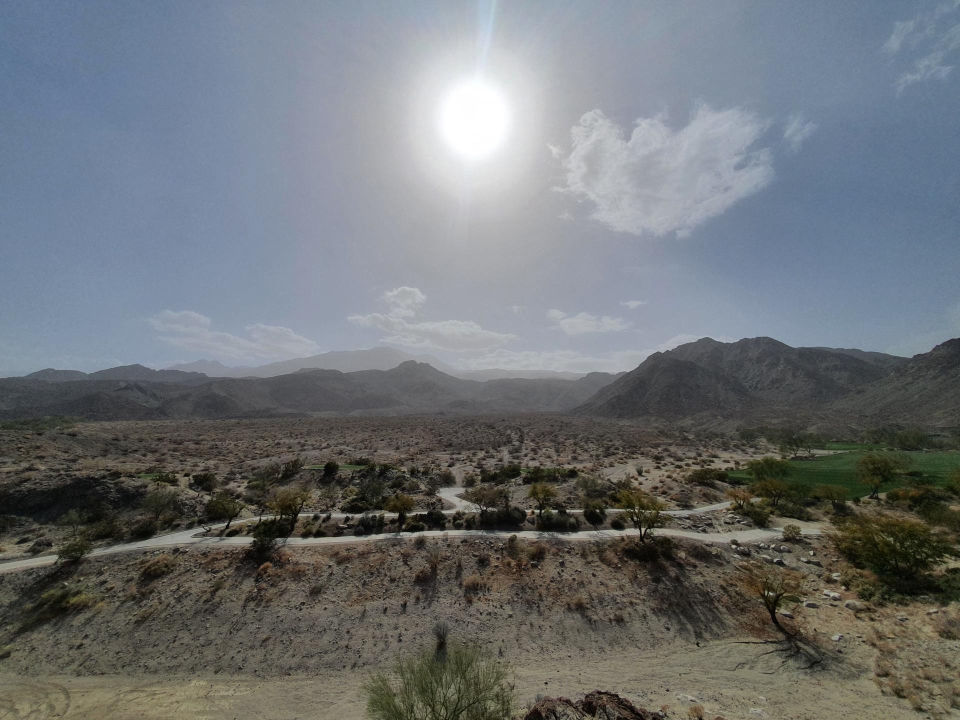 Bright sun shines over a vast desert landscape with distant mountains.