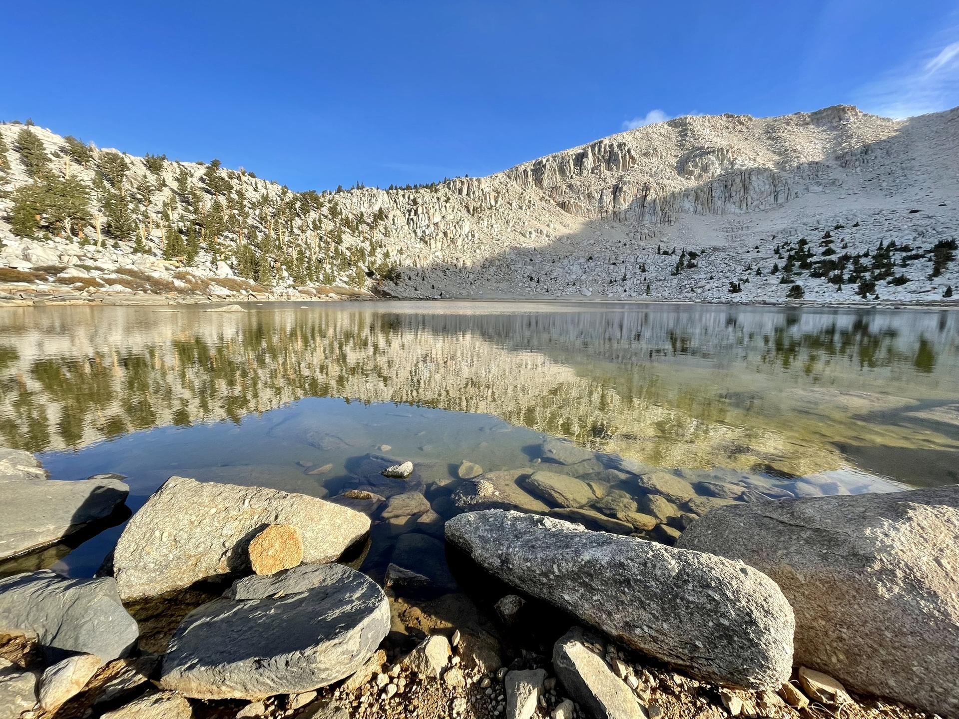 Calm mountain lake reflecting rocky slopes under a clear sky.