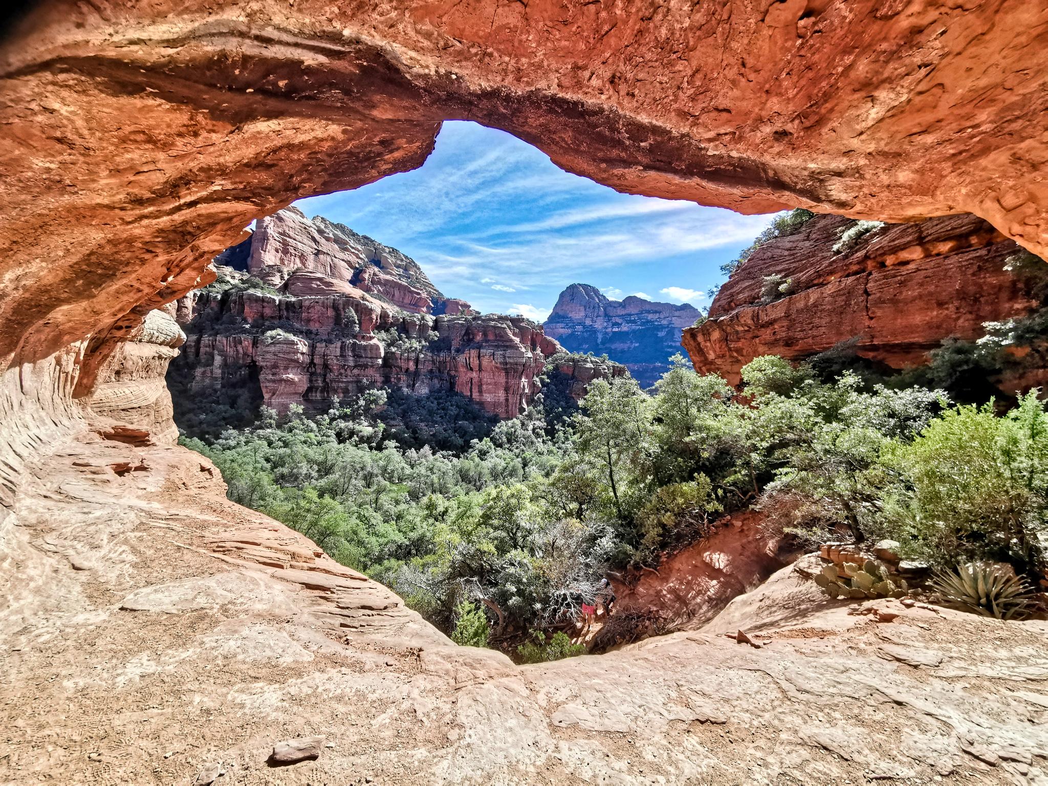 Scenic view through a rock arch of a lush valley and distant mountains.