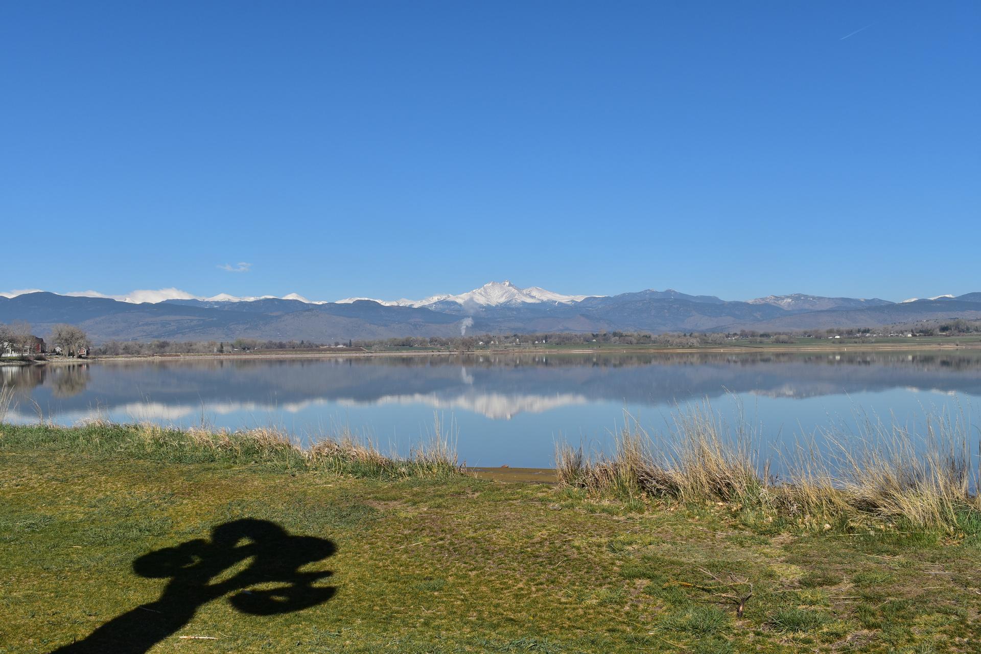 Wide lake reflecting snow-capped mountains under a clear blue sky, sunny.