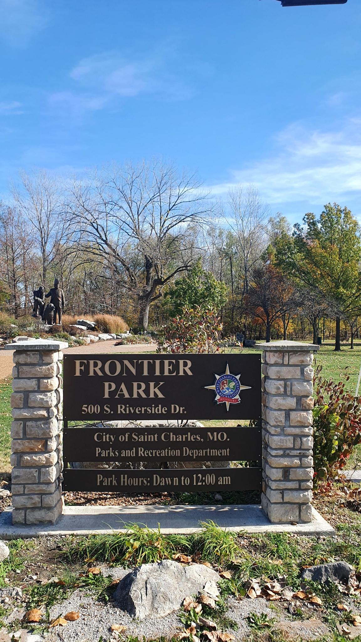 Stone and wood park sign under a clear blue sky with autumn trees.
