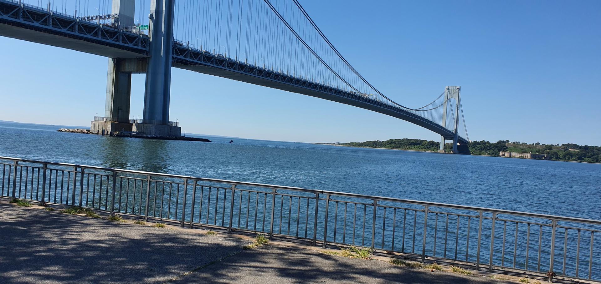 Large suspension bridge over water, with a railing, on a sunny day.