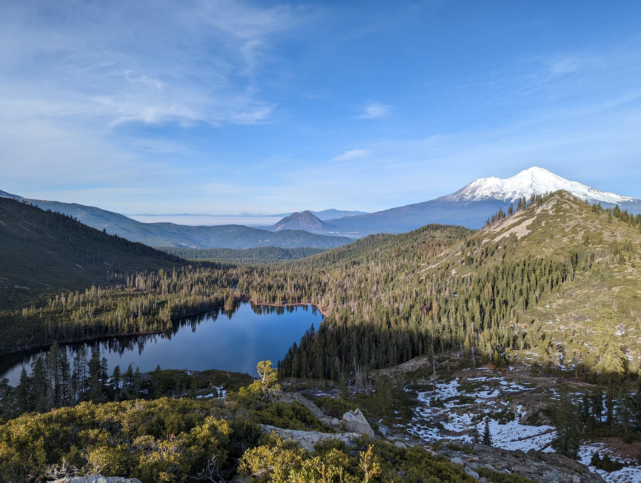Mountain lake surrounded by dense forest, with a snow-capped peak in the distance.