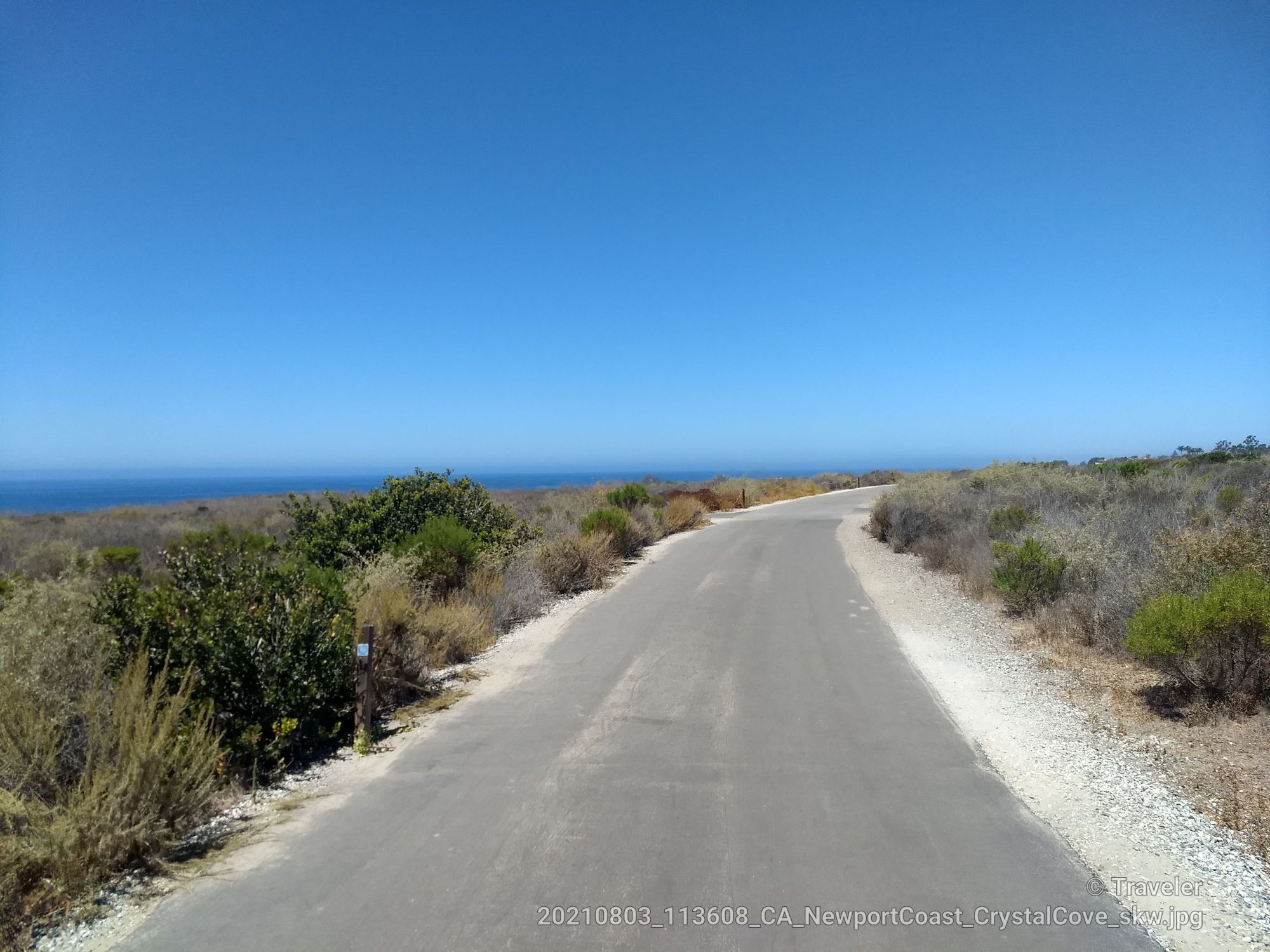 Paved road winding through dry brush towards a bright blue ocean. - Blufftop Multiuse Trail
