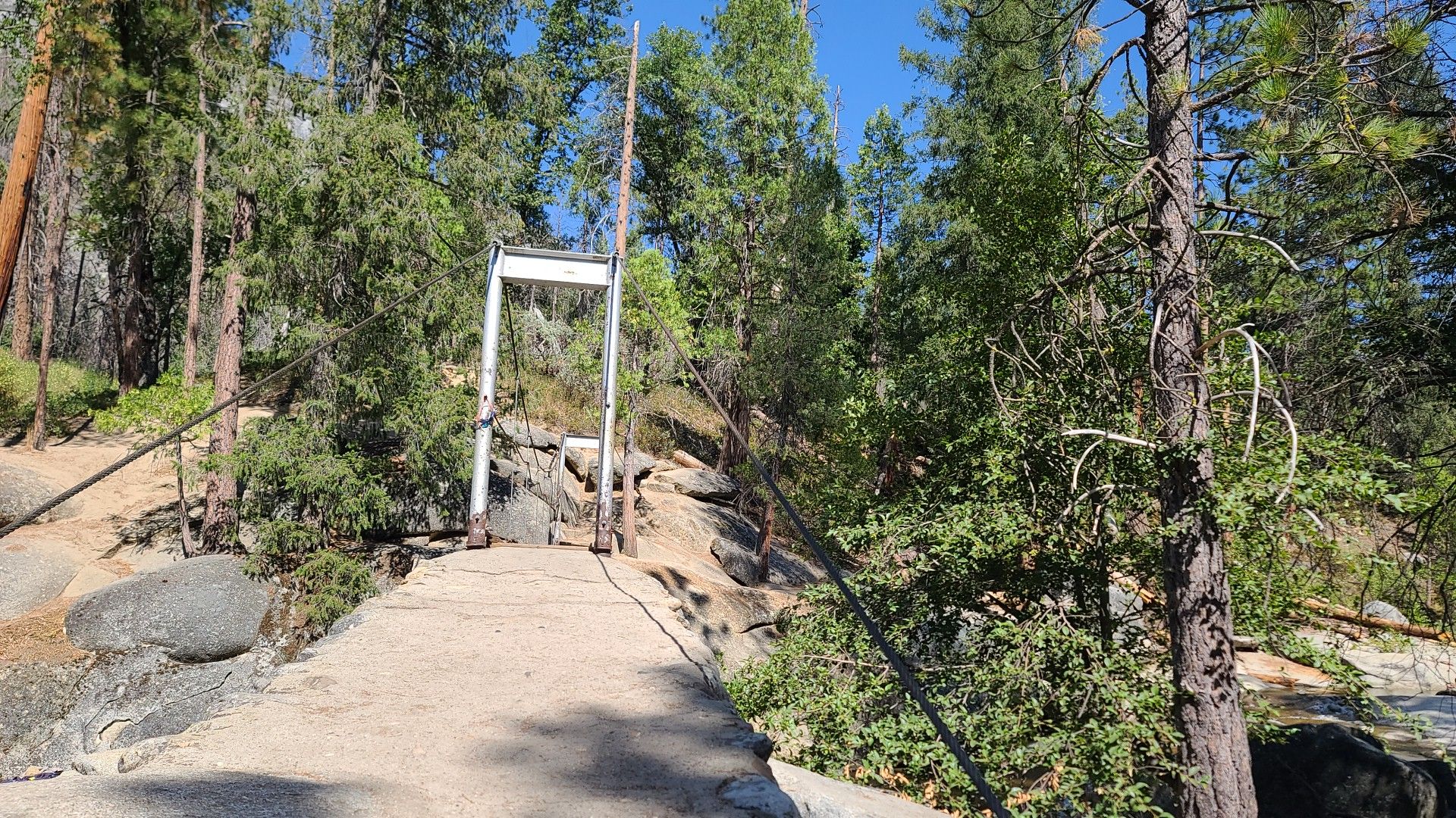 A suspension bridge entrance in a sunny, rocky forest. - Swinging Bridge Loop