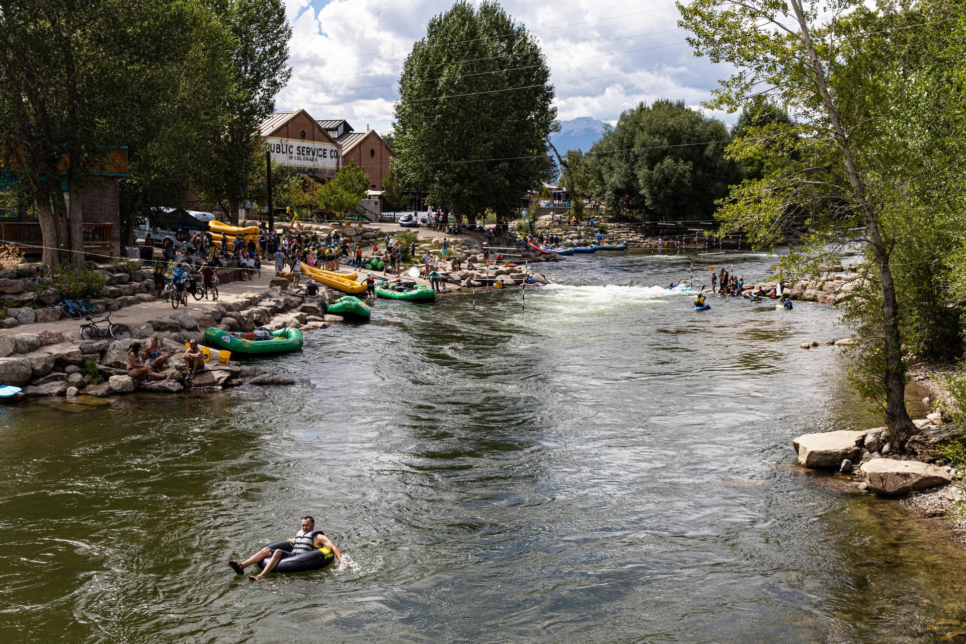 People tube and raft on a wide river under a cloudy sky.