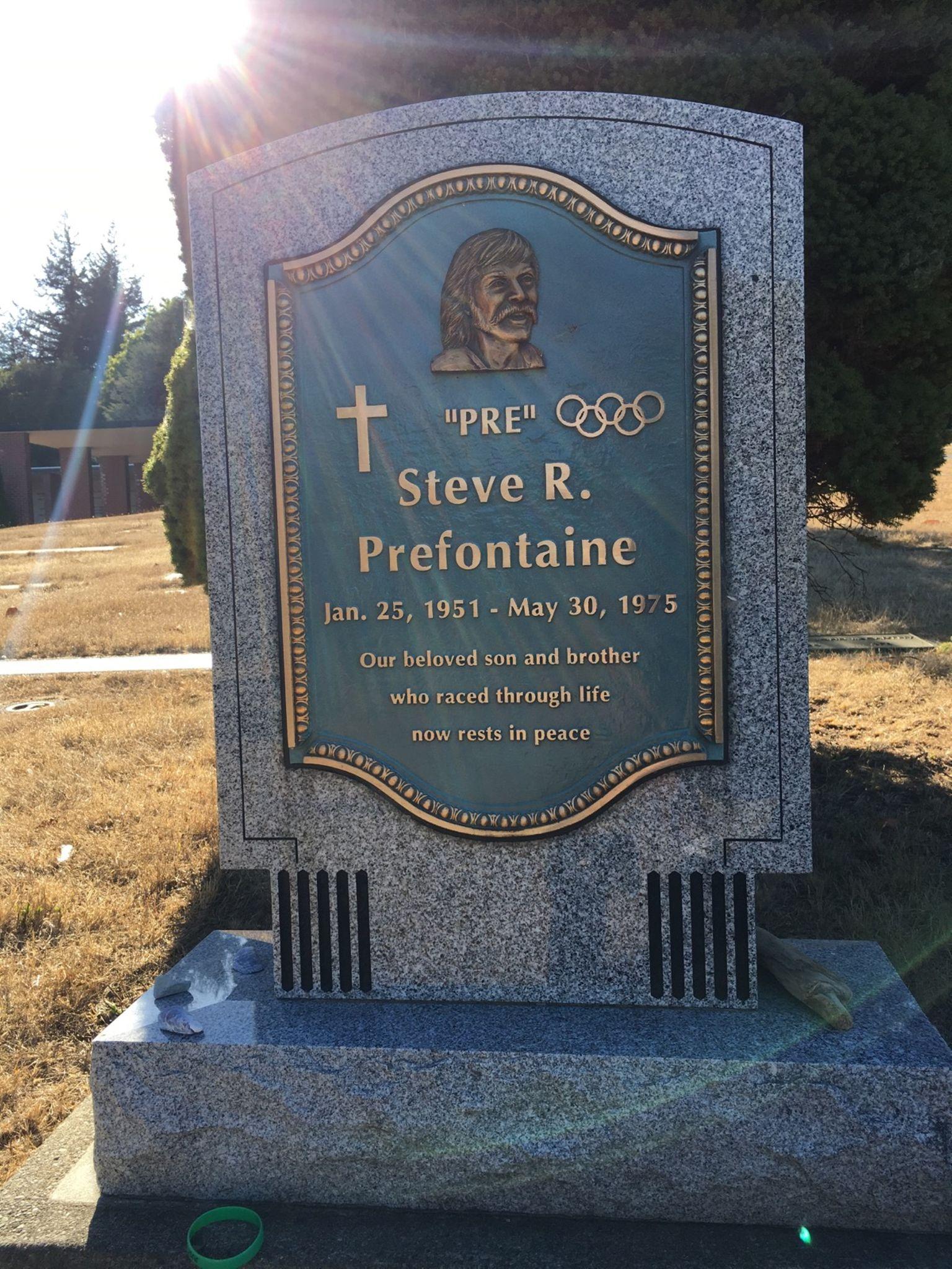 Sunlit granite headstone with a bronze plaque featuring a portrait and Olympic rings.