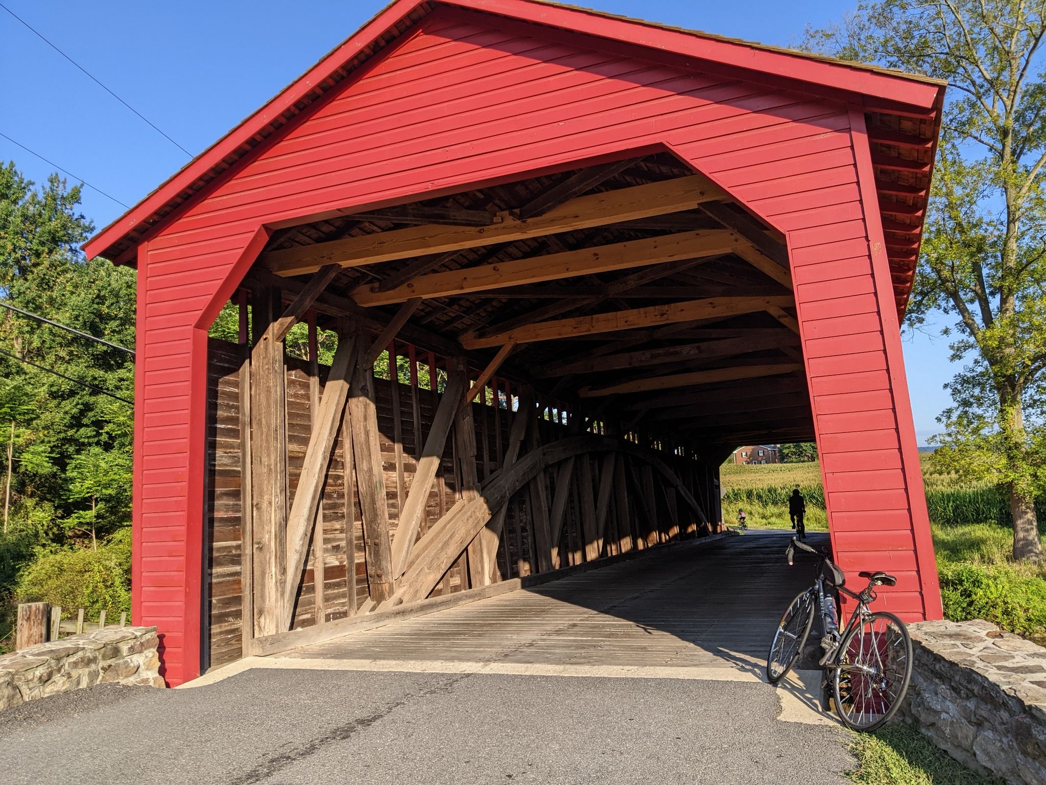 Red covered bridge with a bicycle parked and a person walking inside. - Utica Covered Bridge – Monocacy River loop from Utica