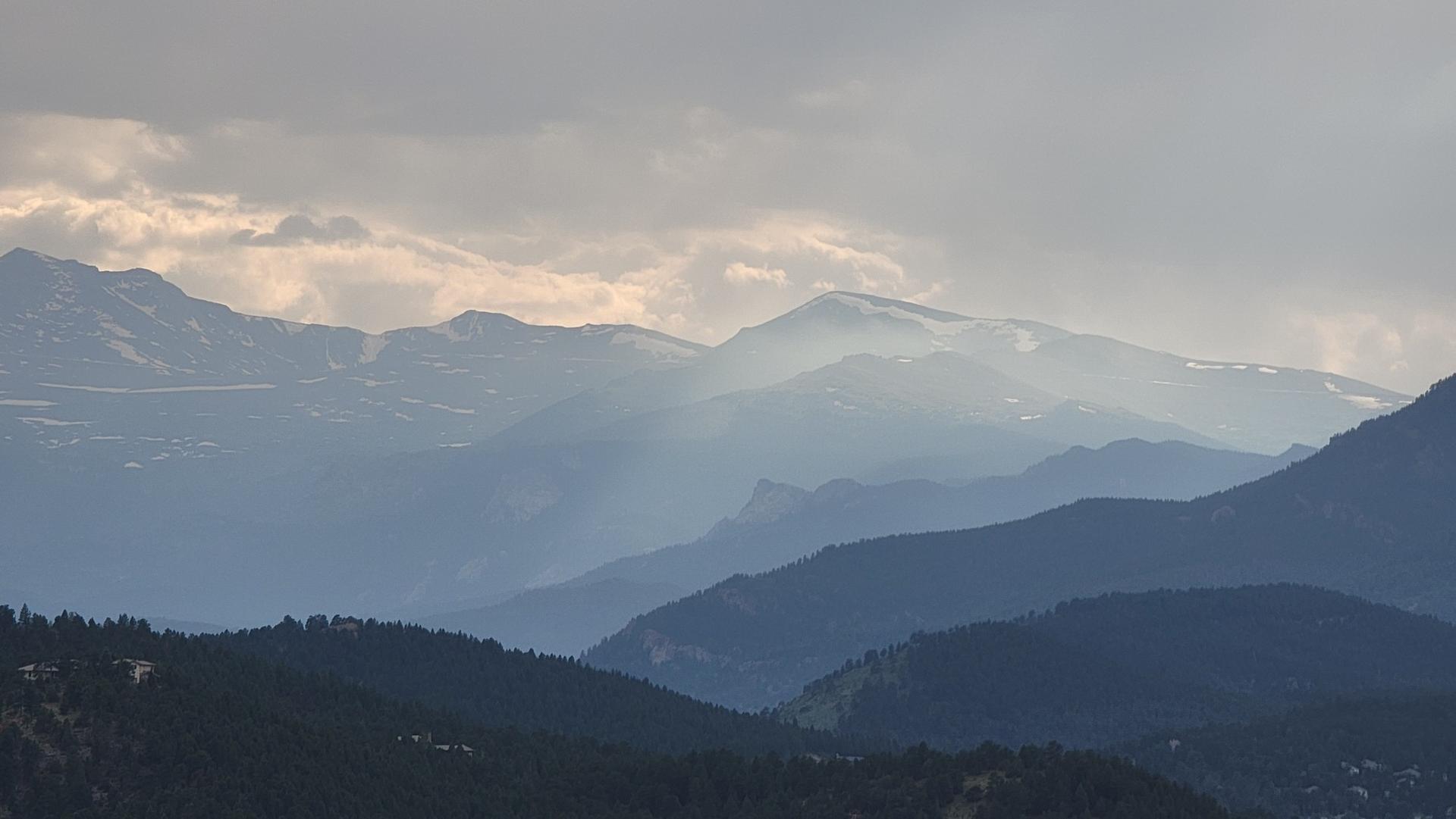 Hazy mountain range with sun rays breaking through cloudy sky.