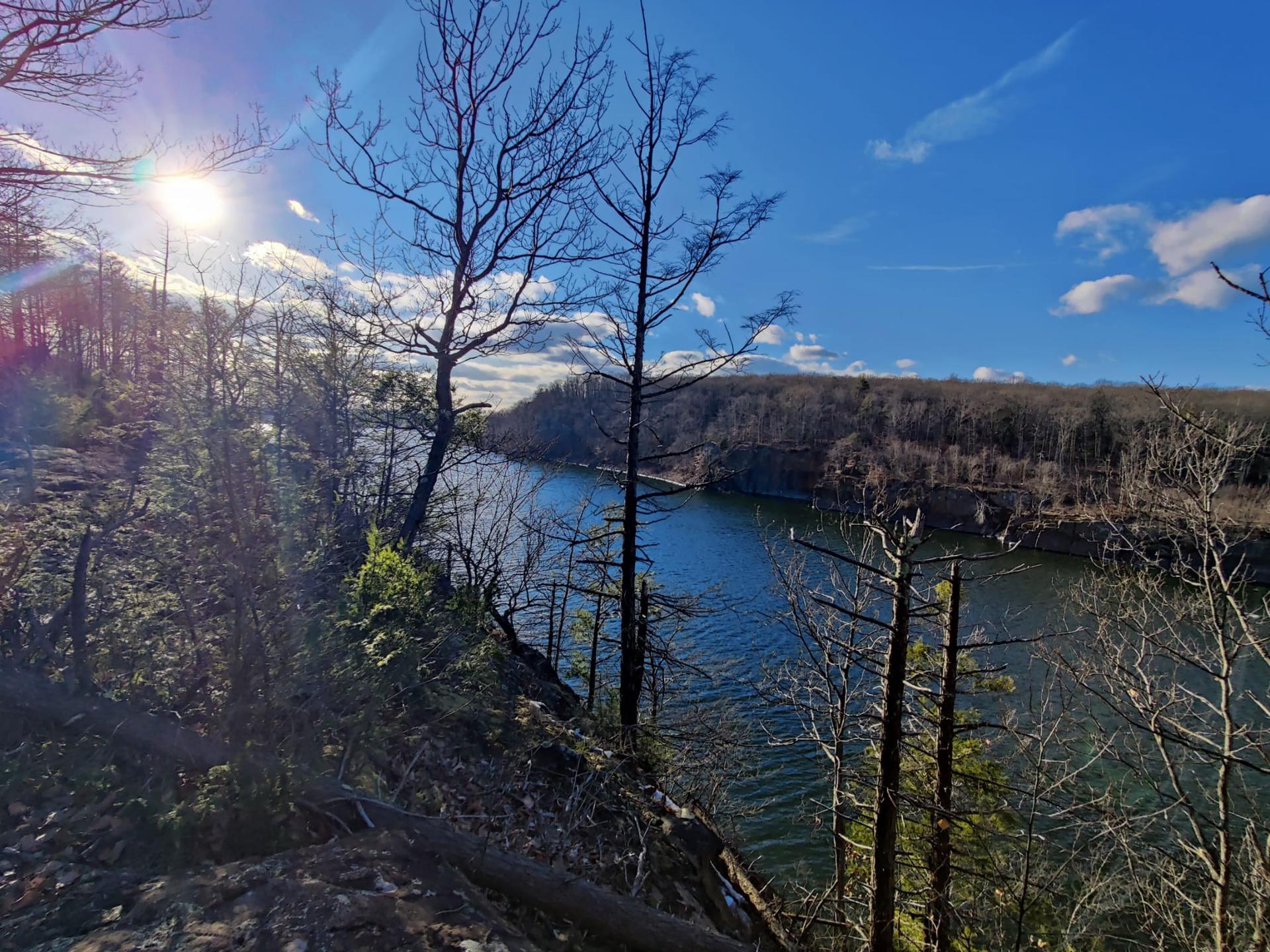 Bright sun over a wide river with bare trees on forested banks.