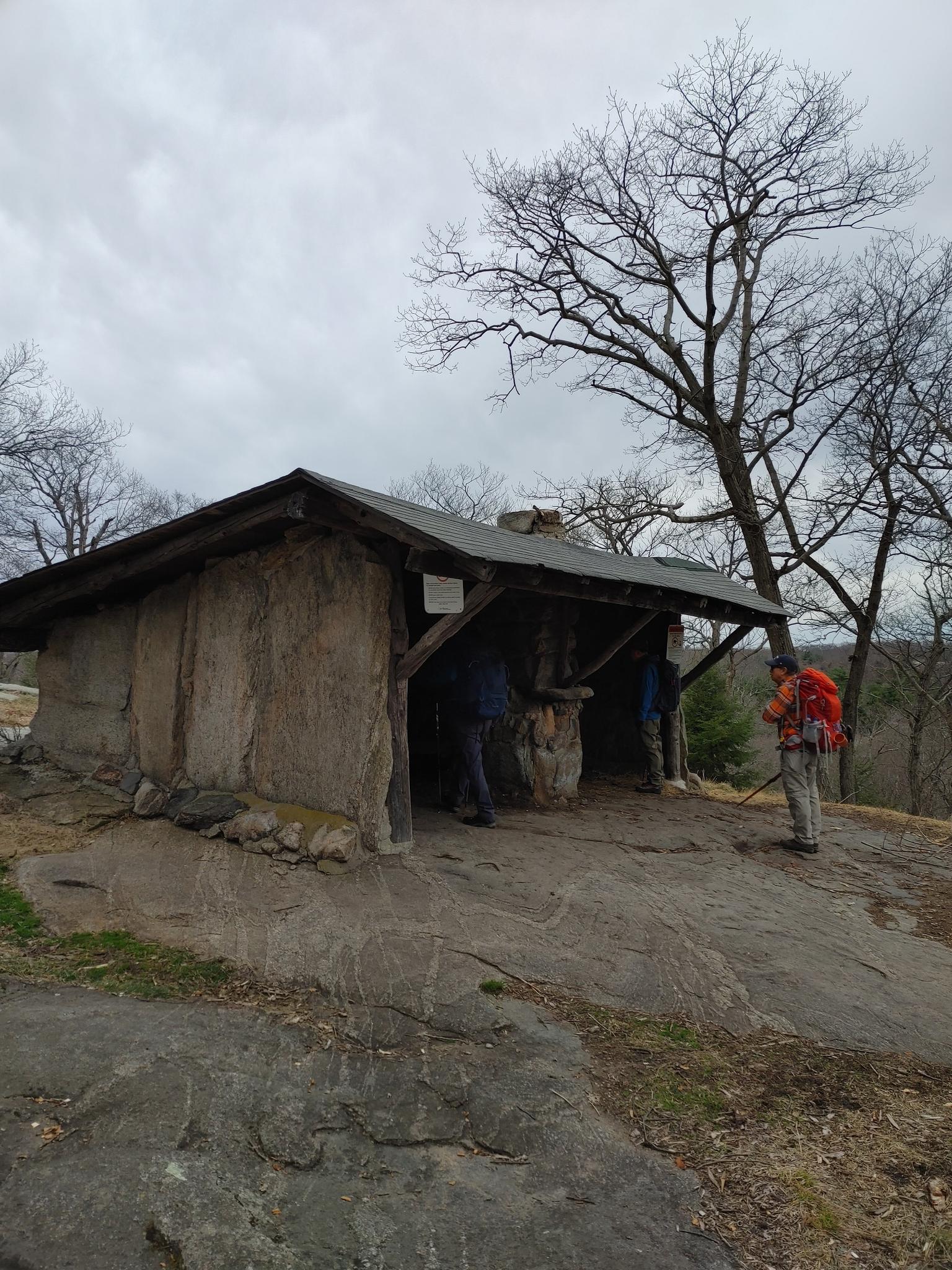 Hikers at a rustic stone shelter under a cloudy sky.