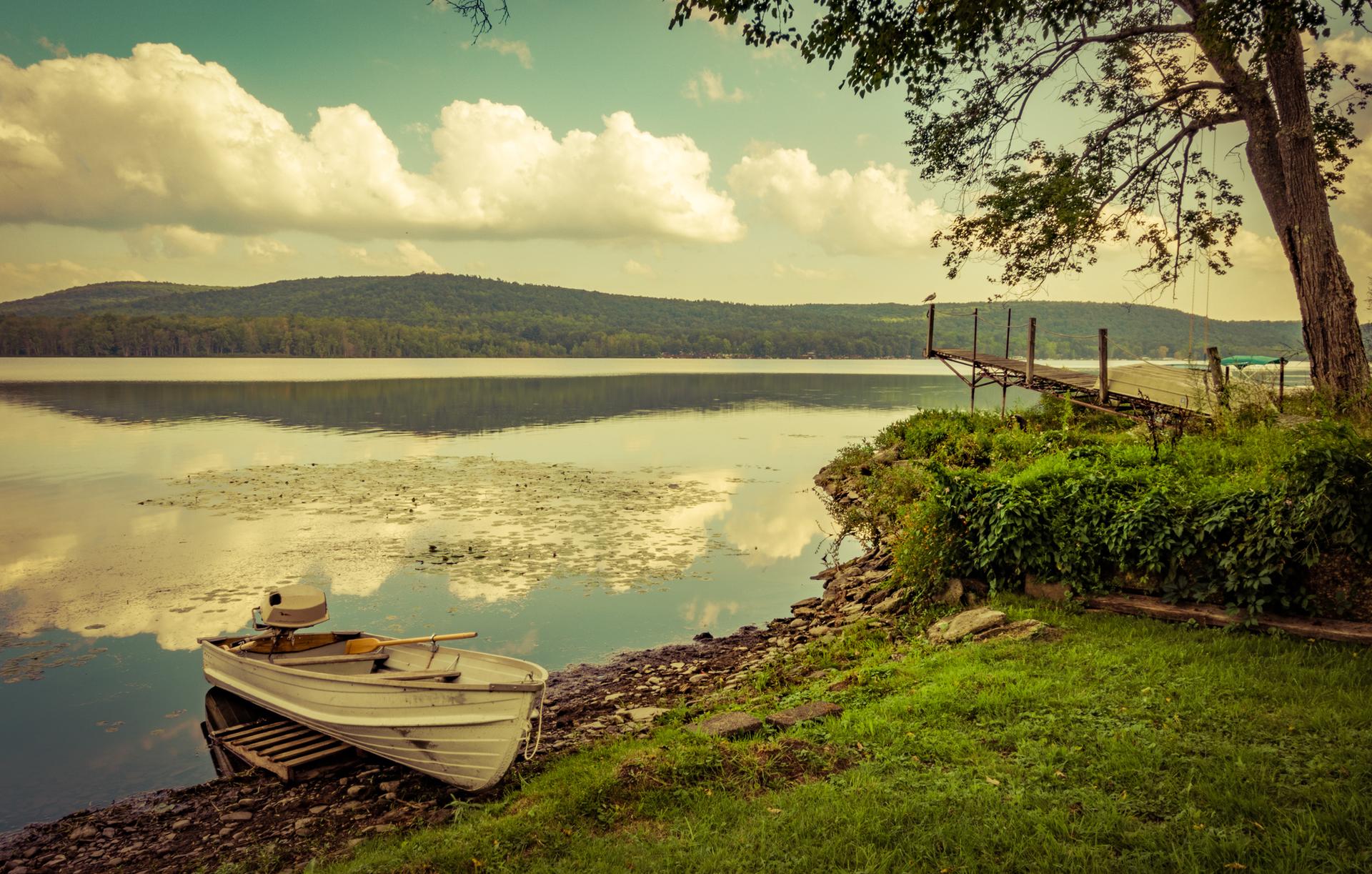 Small boat on a calm lake shore with a dock and green trees.